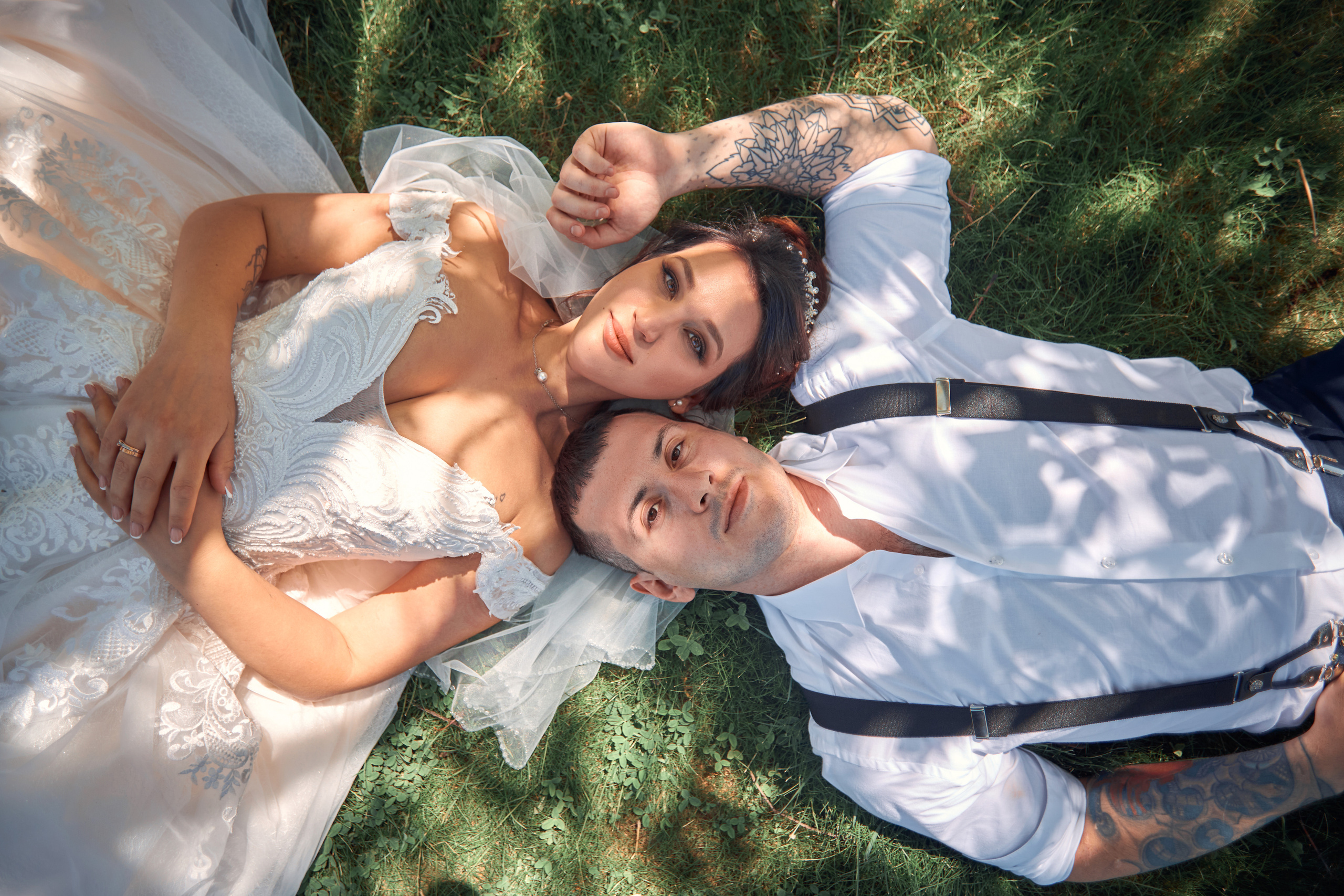 Молодожены лежат на газоне и смотрят в камеру