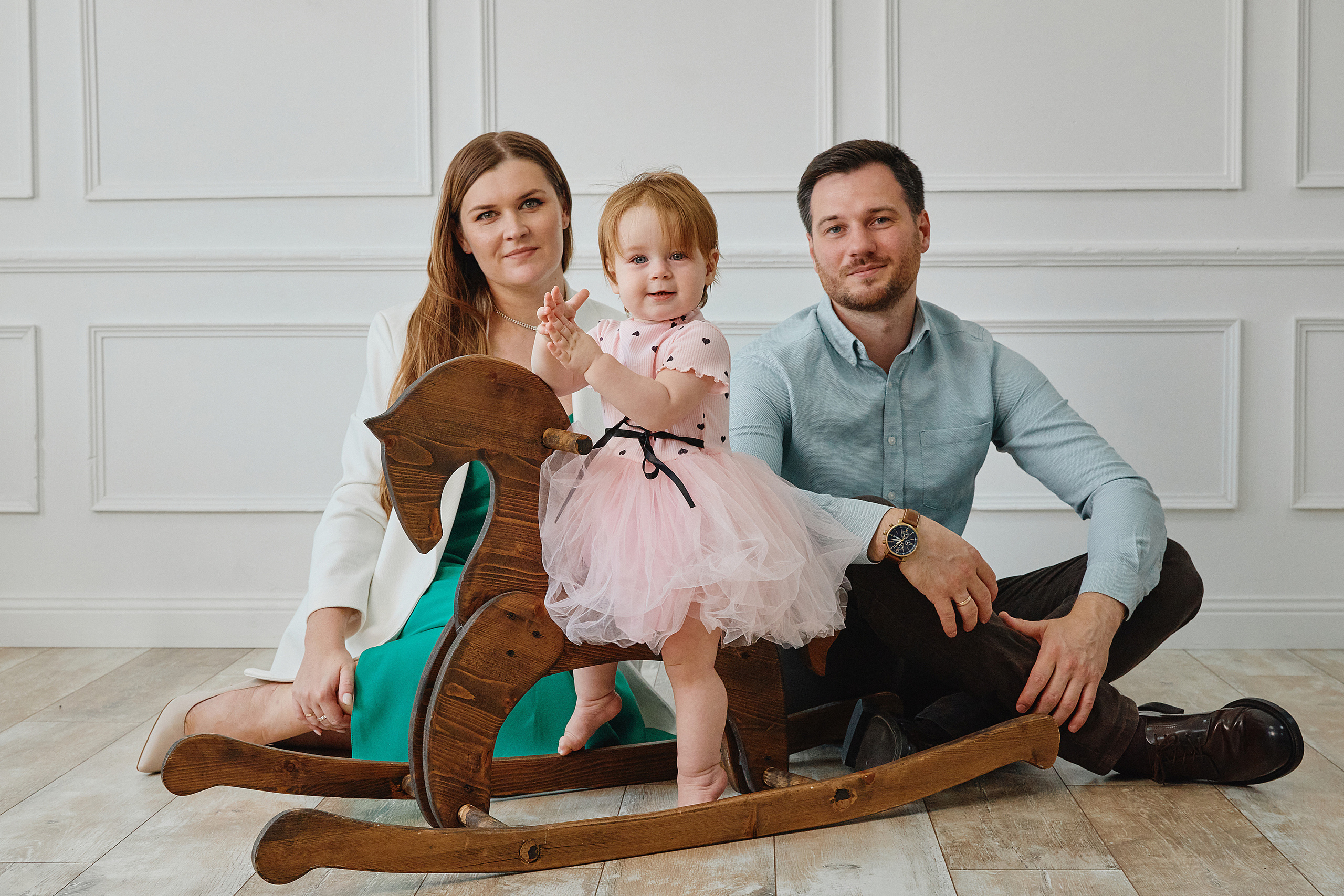 Ребенок катается на деревянной лошадке на фоне родителей