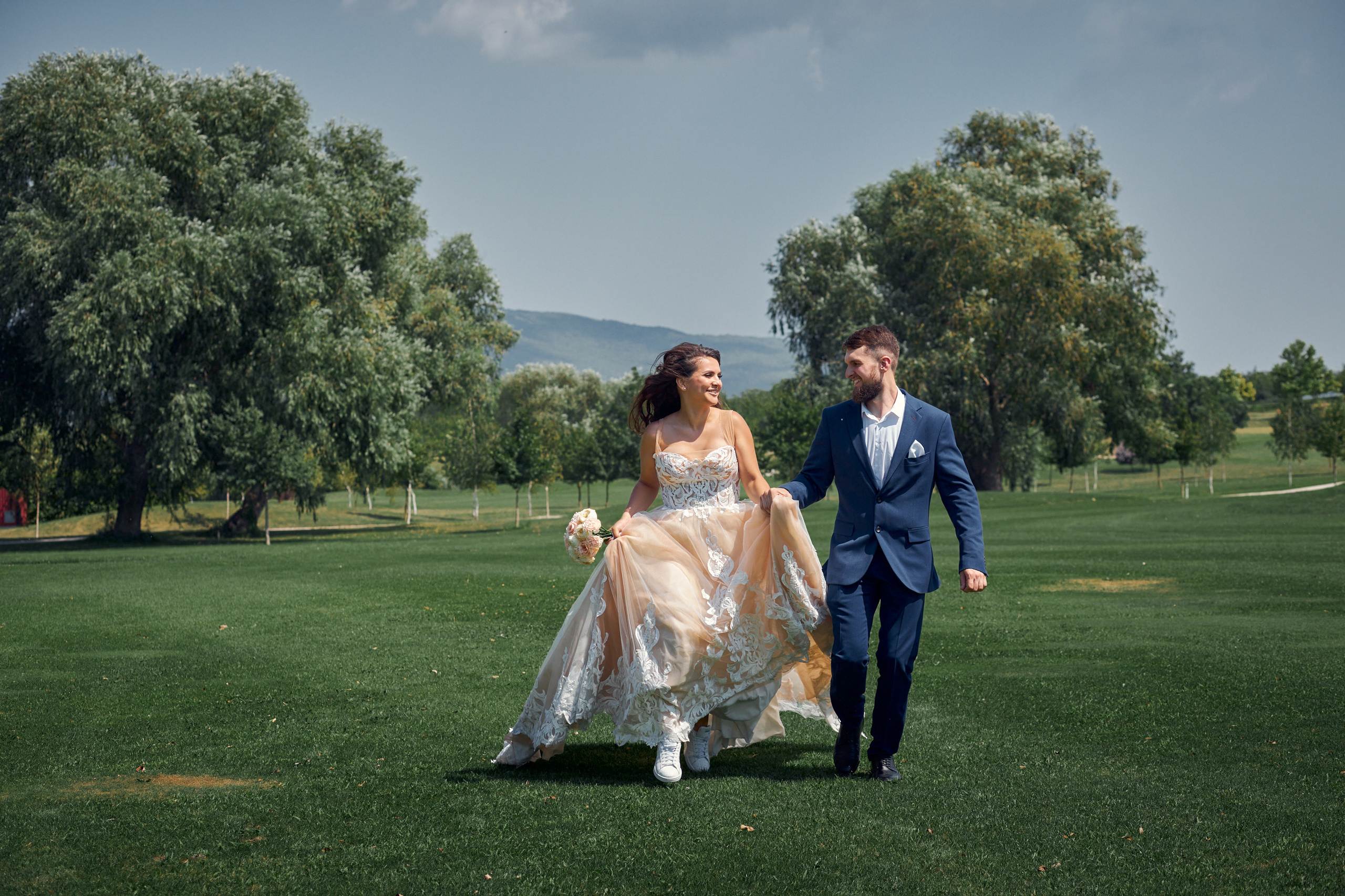 Молодожены бегут по зеленому полю и улыбаются друг другу