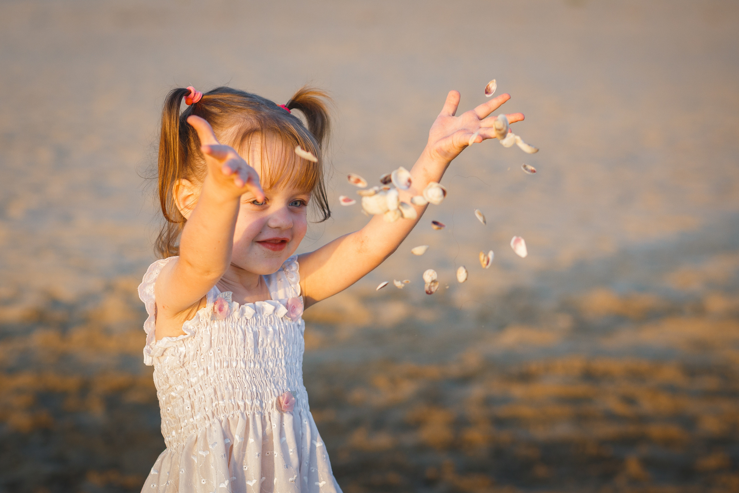 Девочка разбрасывает ракушки на пляже