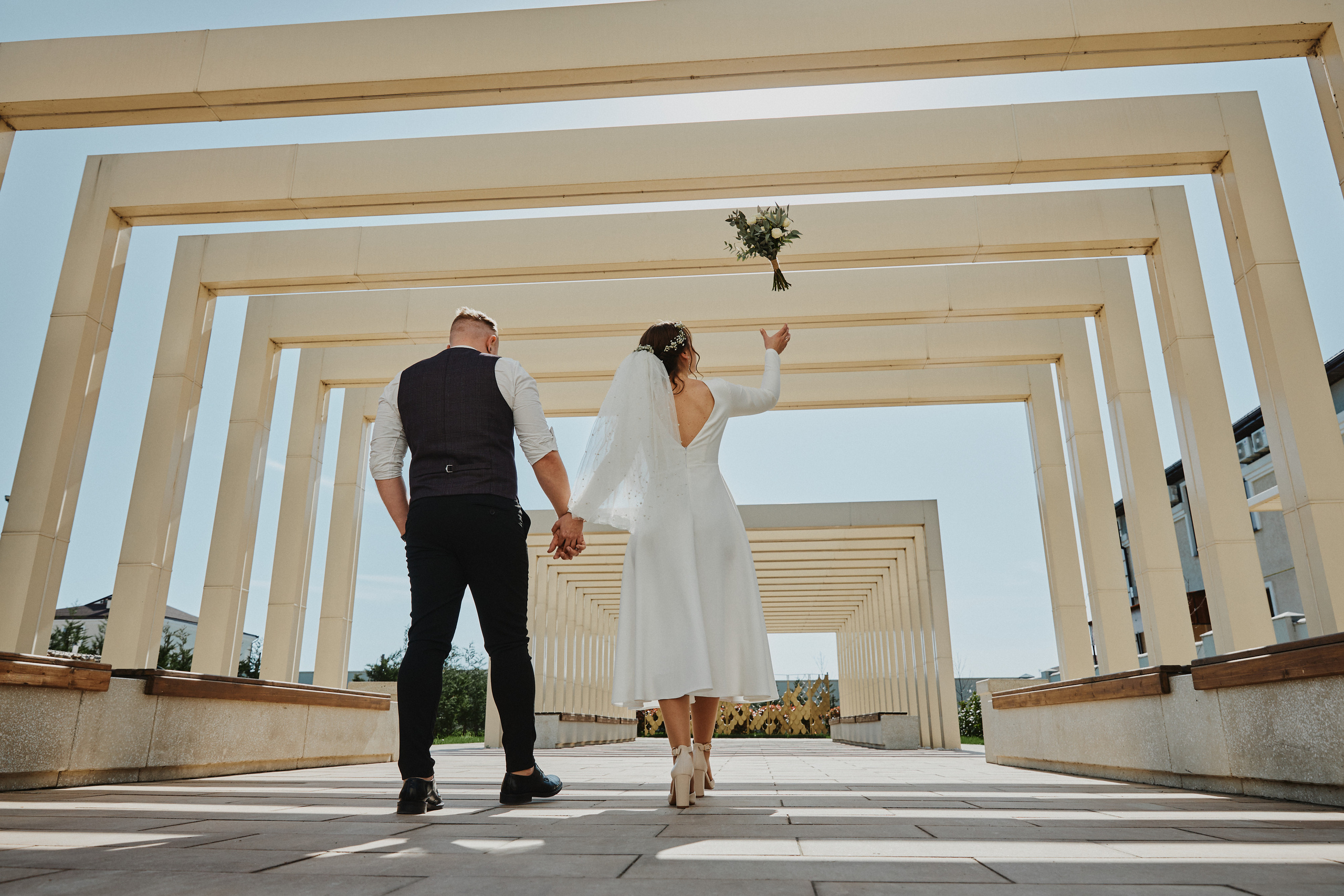 Невеста идет с женихом за руки и подбрасывает букет невесты