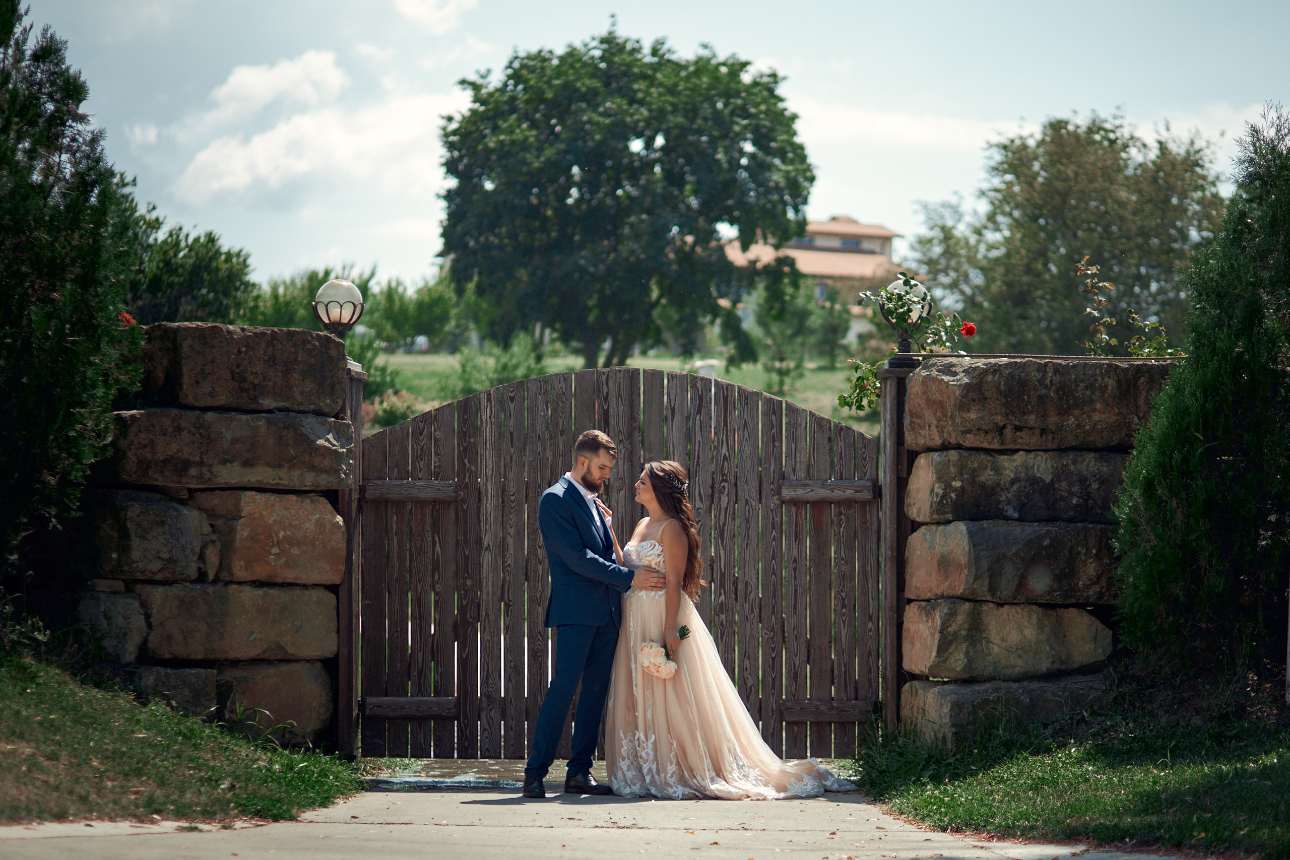 Молодожены стоят возле старых ворот на фоне зелени