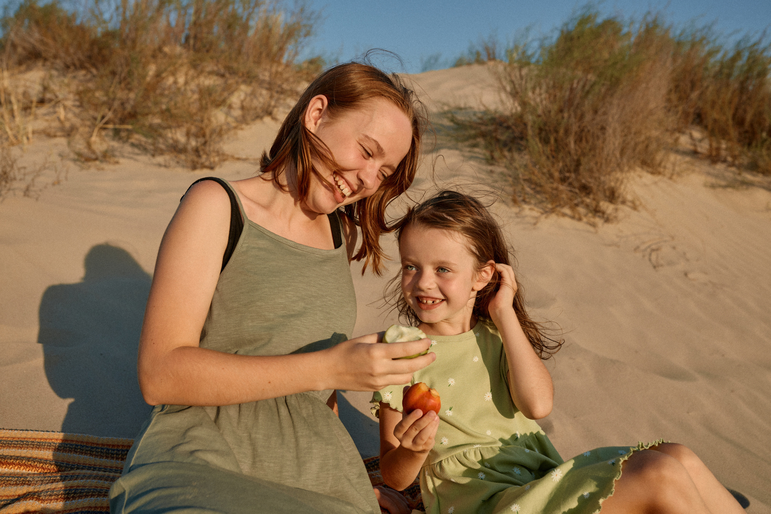Сестры улыбаются и смеются в песчаных дюнах на пляже