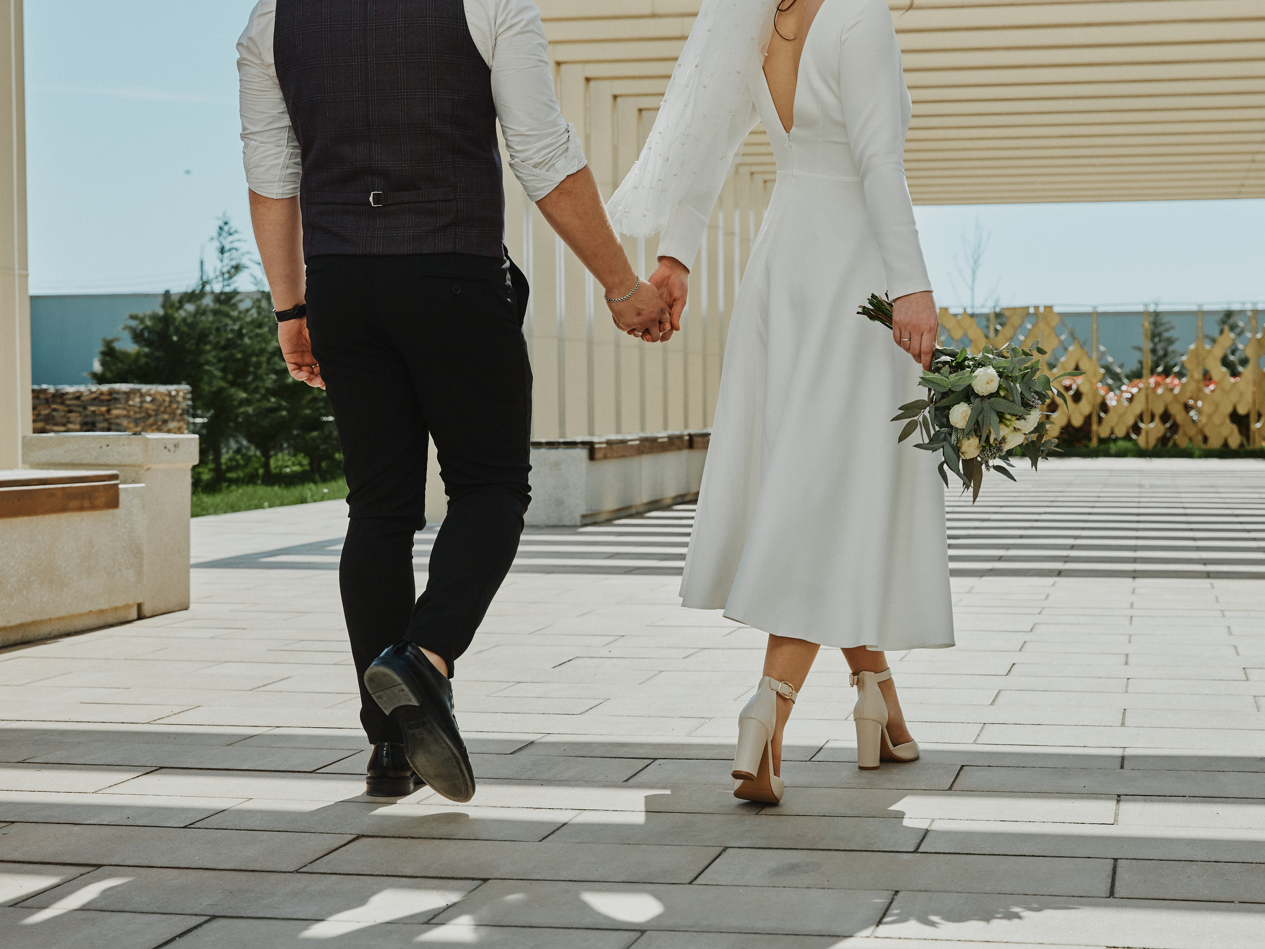 Жених с невестой идут держась за руки спиной к камере