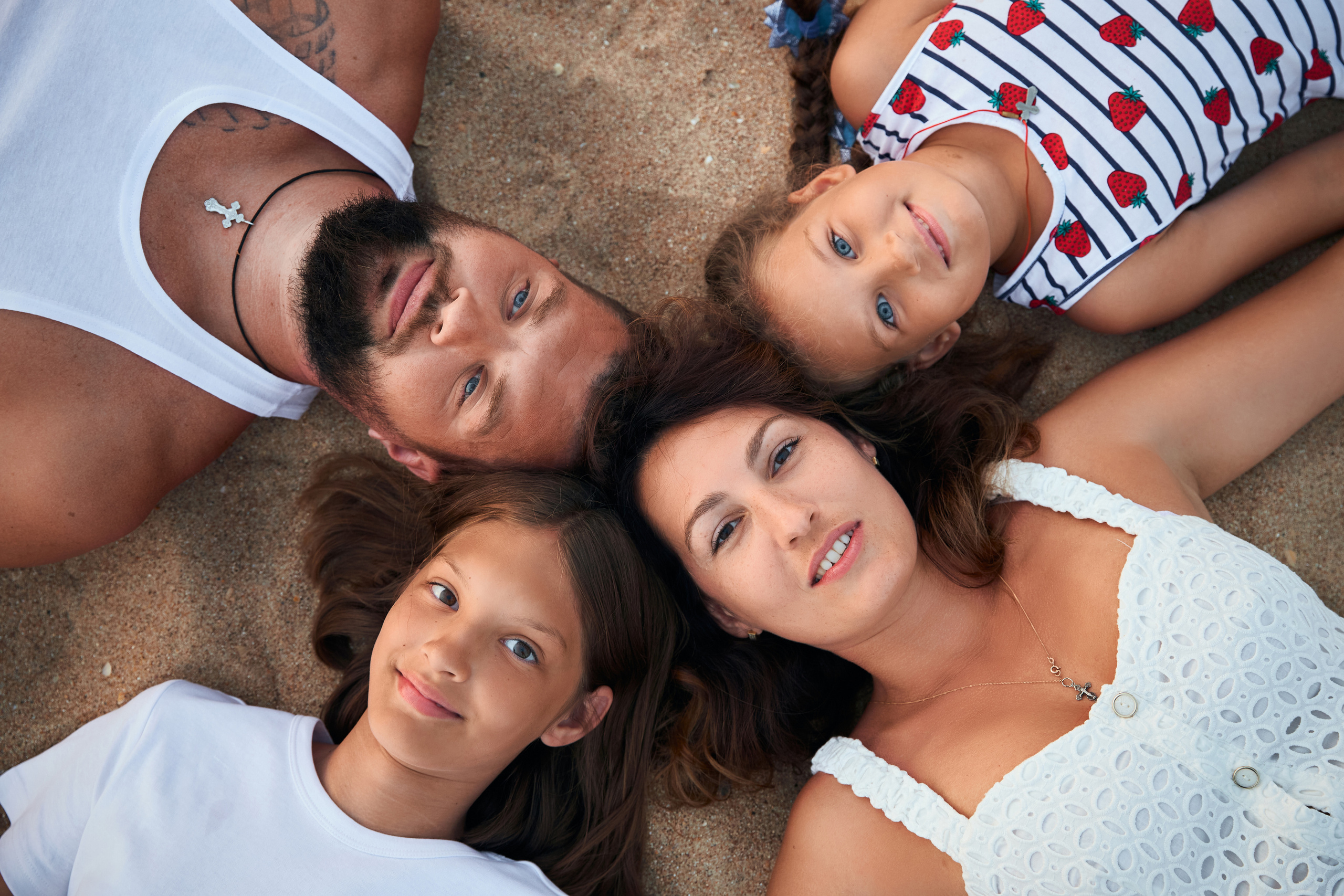 Семья лежит на пляже на песке и все смотрят в камеру