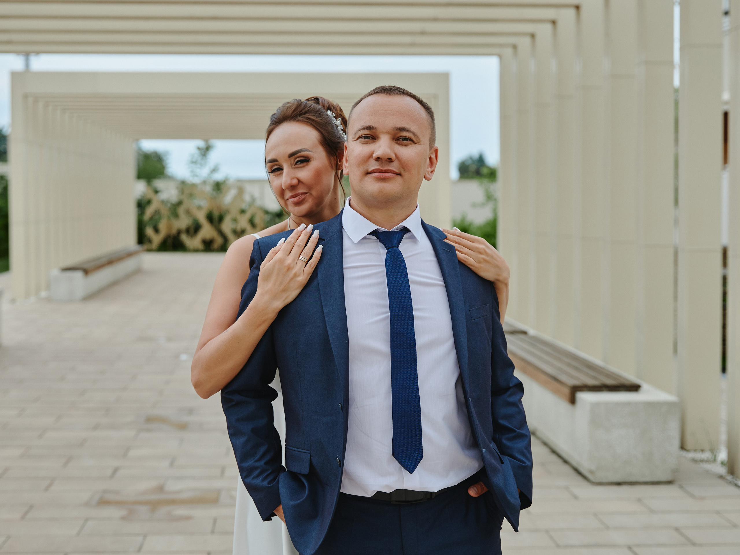 Невеста обнимает жениха за плечи сзади и улыбается