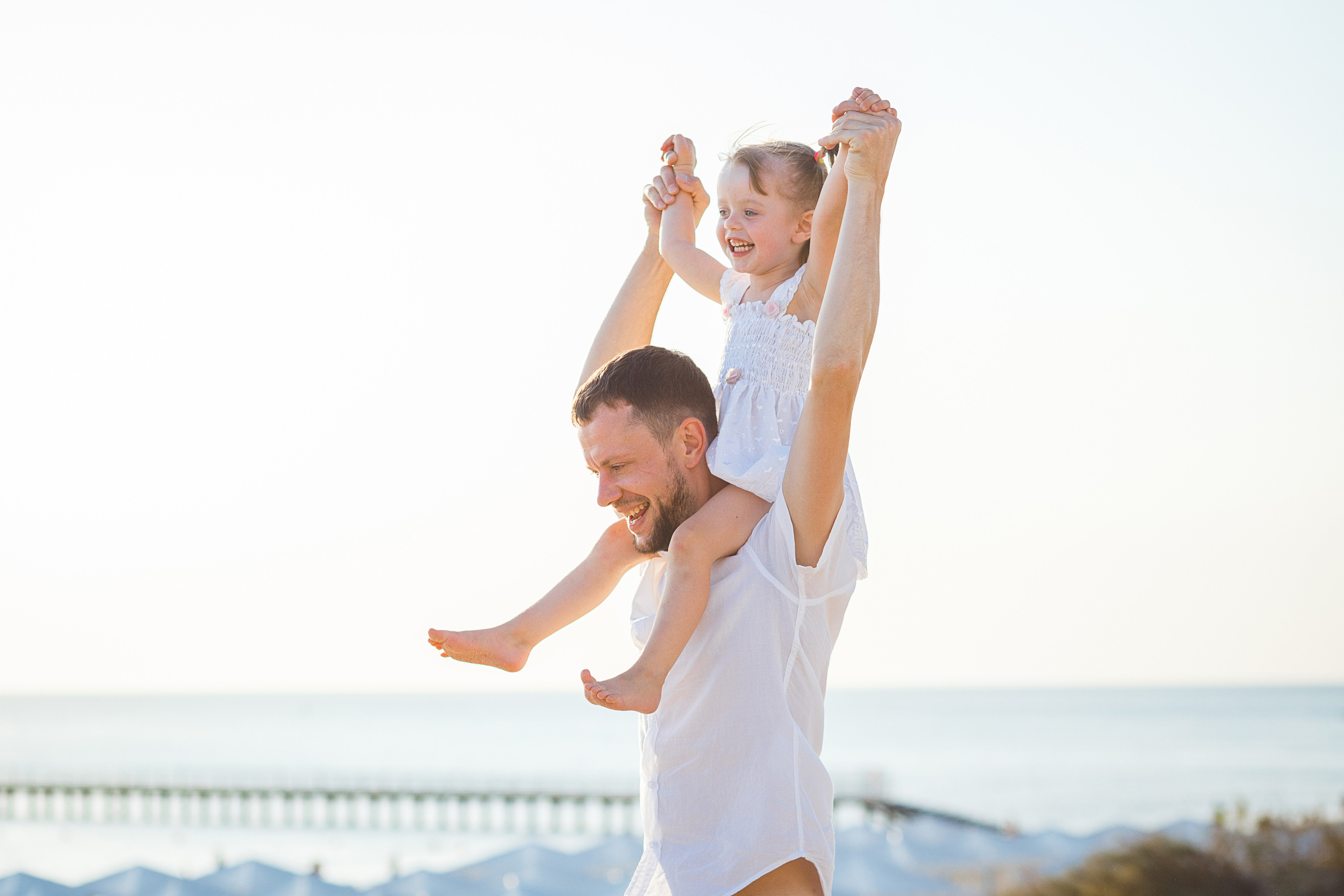 Дачка сидит у папы на плечах и улыбается на берегу моря