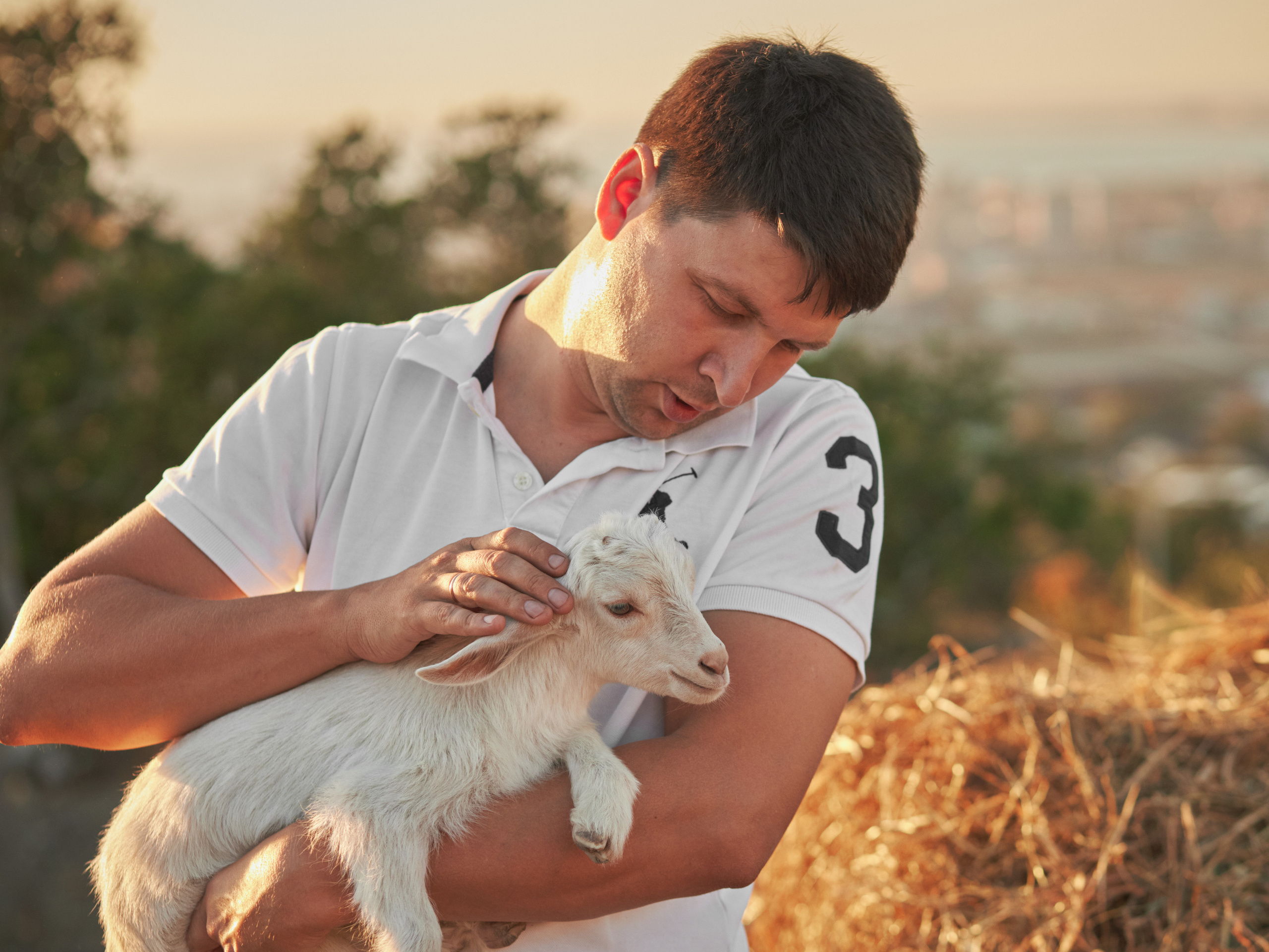 Парень гладит козленка держа его на руках