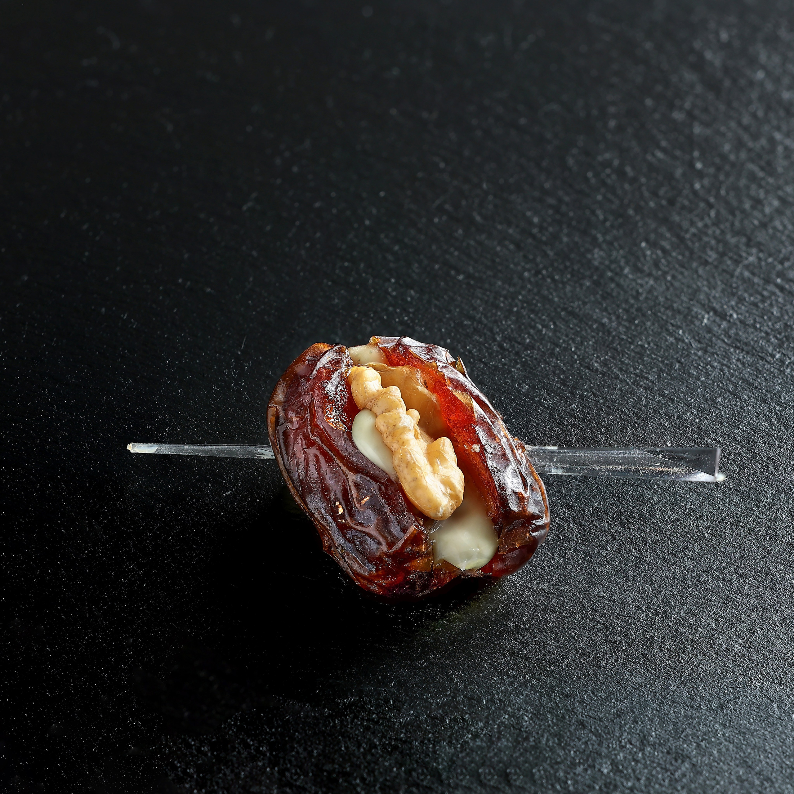 Финик с крем-сыром и грецким орехом, проткнутый декоративной шпажкой.