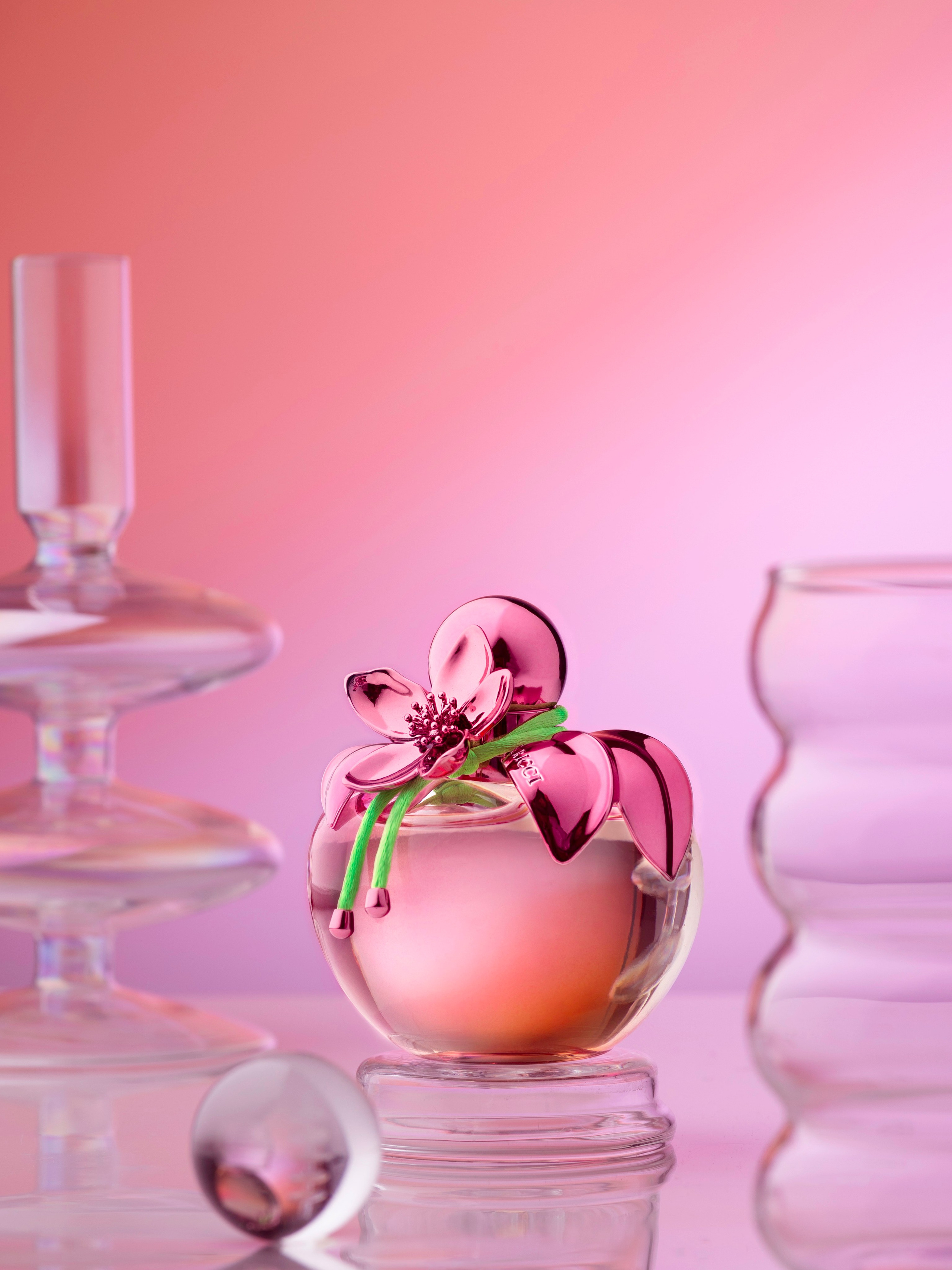 Парфюмерная вода Nina Ricci на розовом фоне со стеклянными подсвечником и стаканами