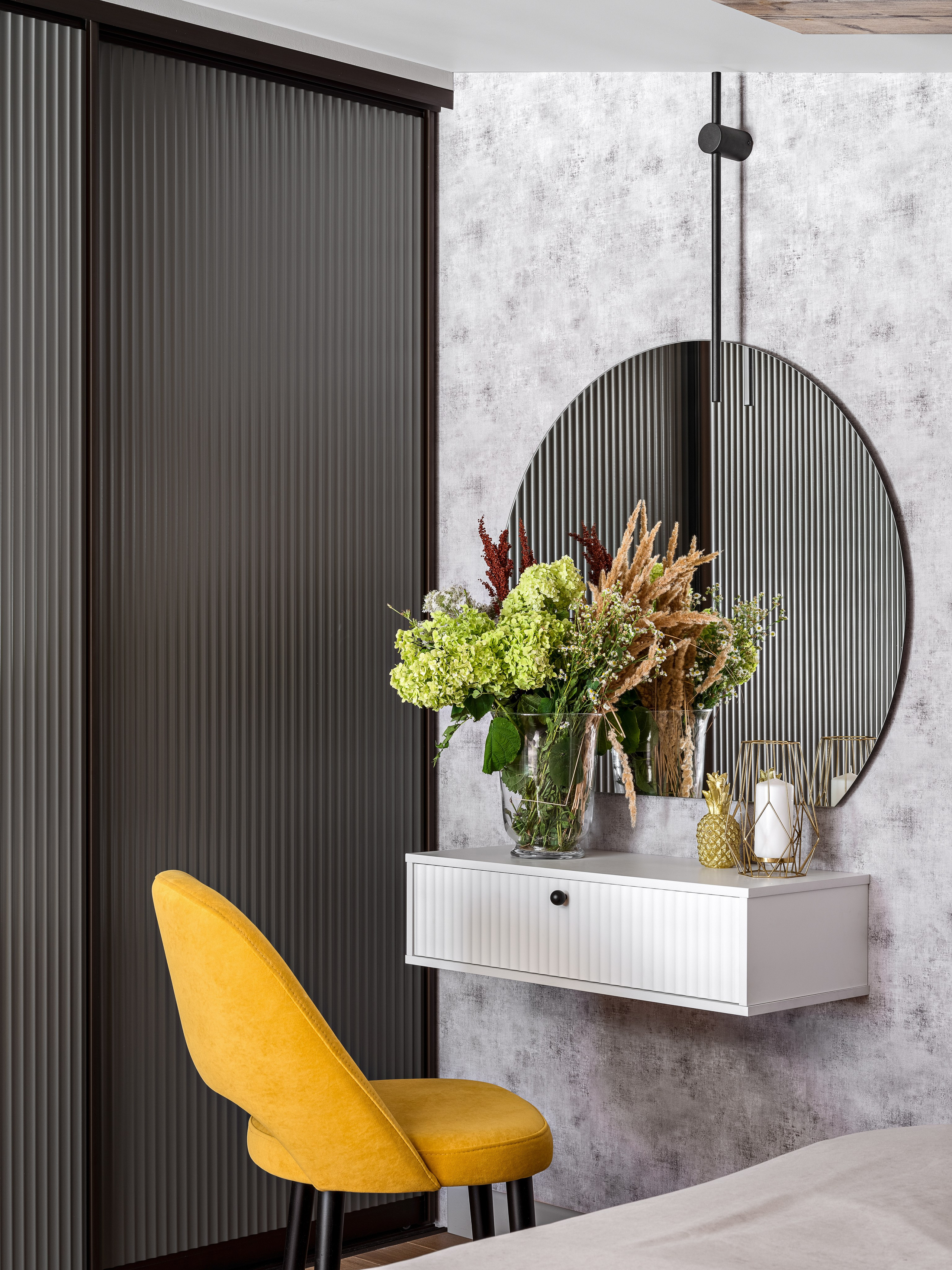 Туалетный столик с круглым зеркалом, ярким жёлтым креслом и декоративными аксессуарами, часть уютного интерьера спальни, реализованного Алёной Поповой и Анастасией Дмитриевой, снятый фотографом Сергеем Денисенко.