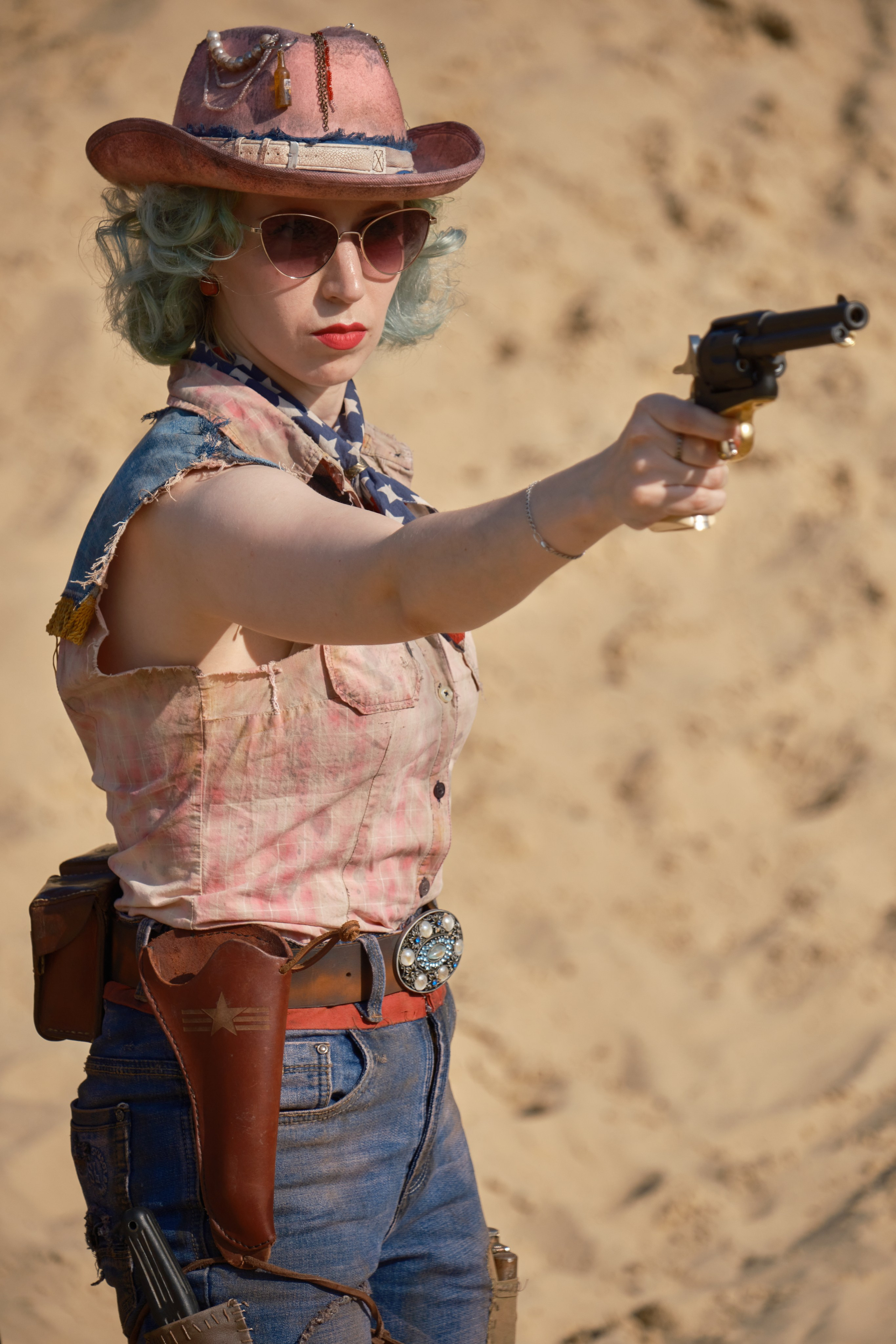 Девушка в розовой шляпе и очках целиться из револьвера в стиле пост апокалипсис