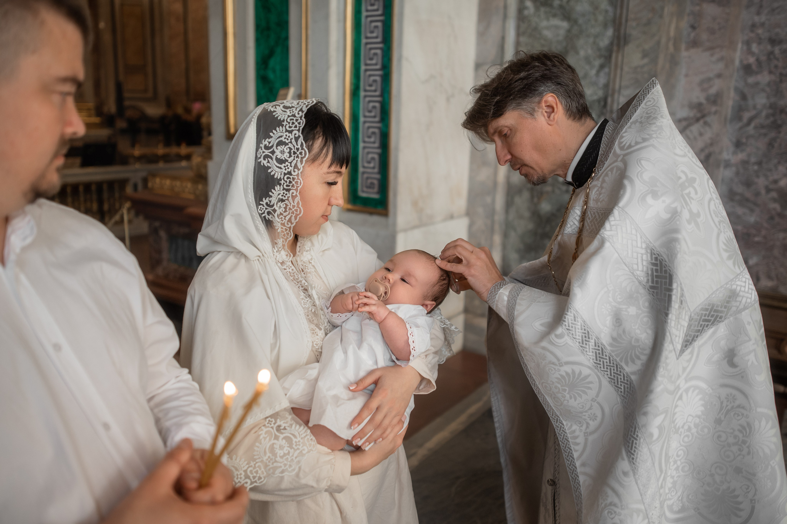 священник постригает волосы младенцу во время крещения