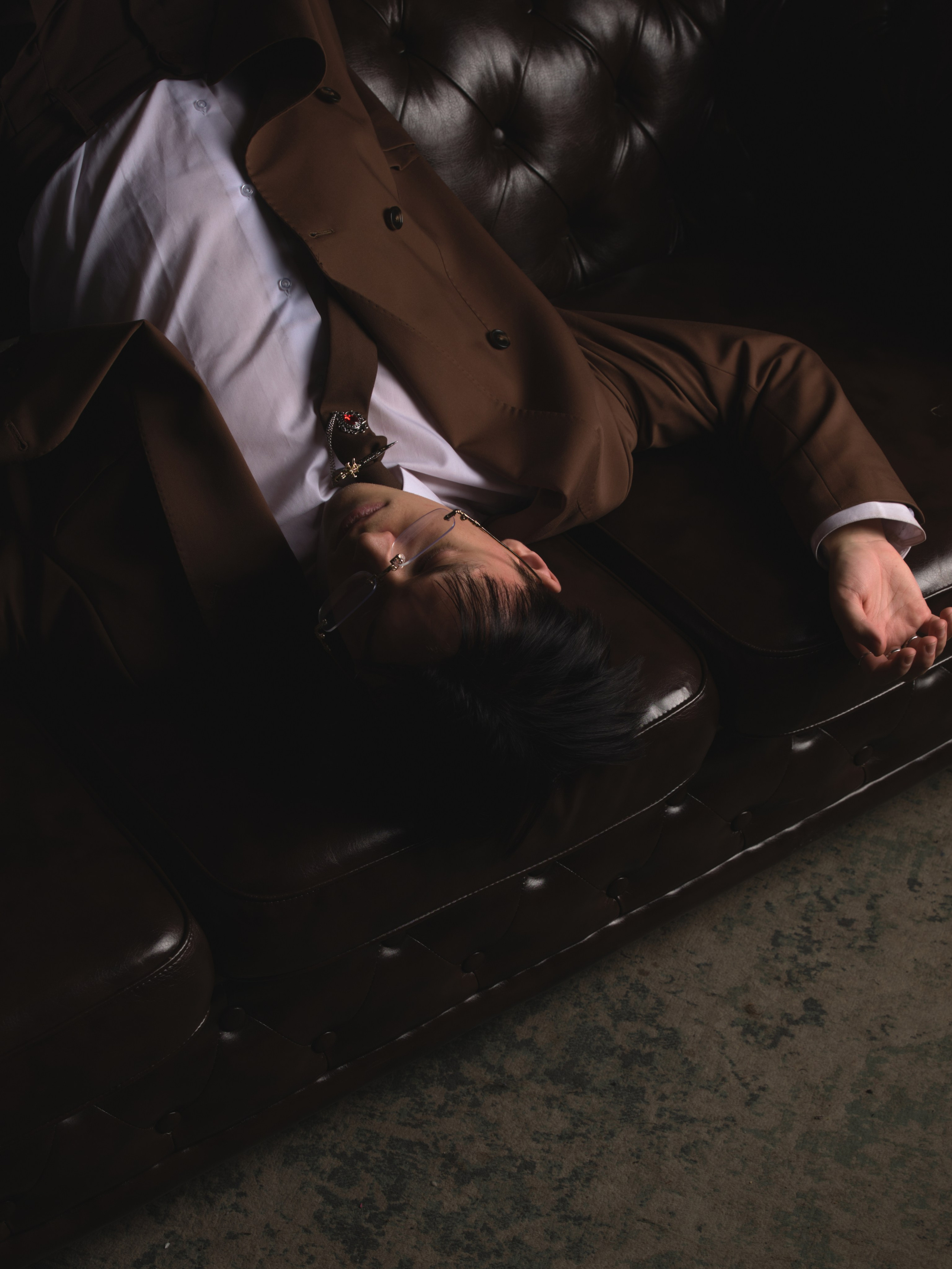 молодой парень костюме оверсайз лежит на диване в необычной позе