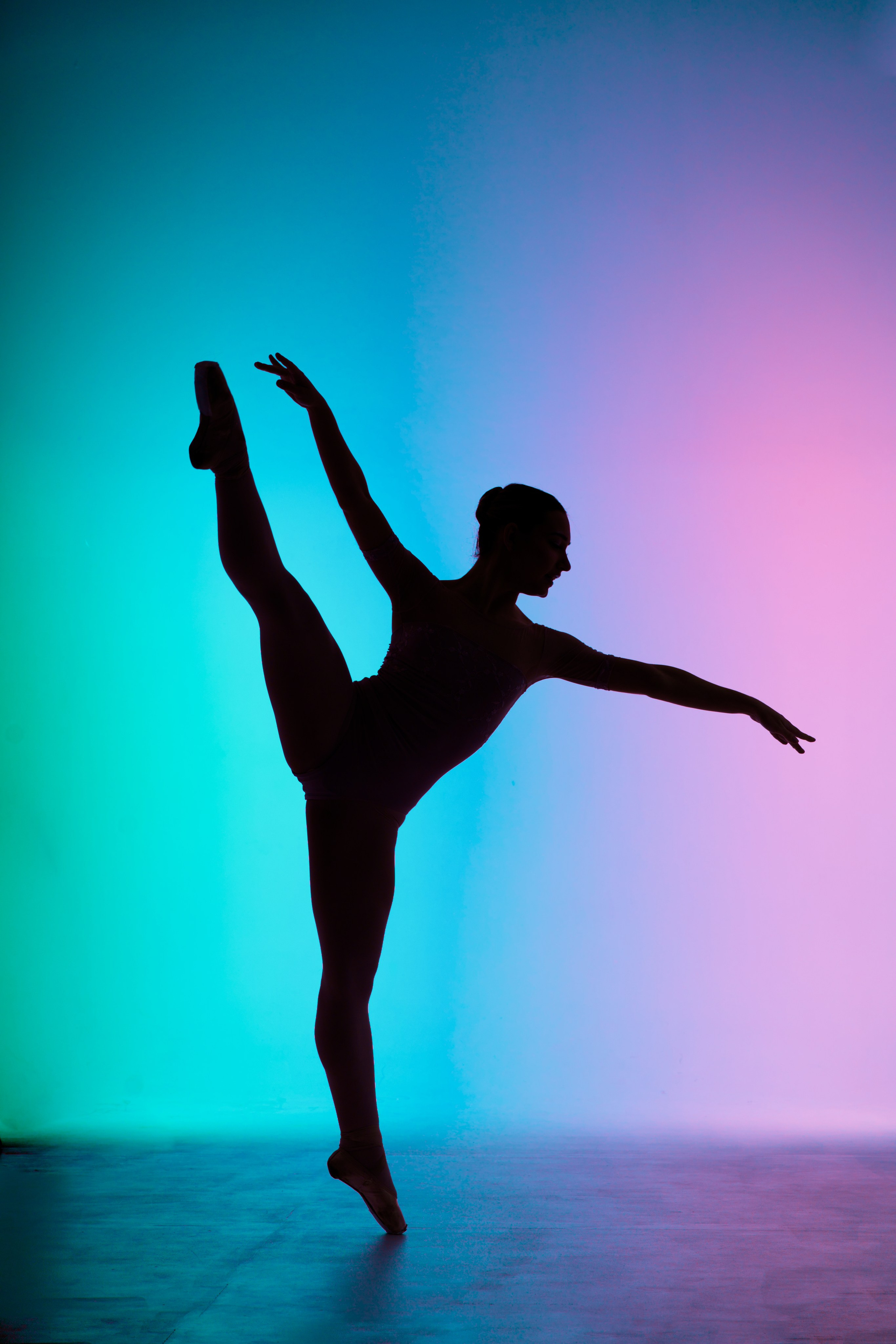 Силуэт балерины в высоком вертикальном шаге (гранд батман) на фоне неонового градиента. Профессиональное портфолио танцора, акцент на чистоте линий и технике.