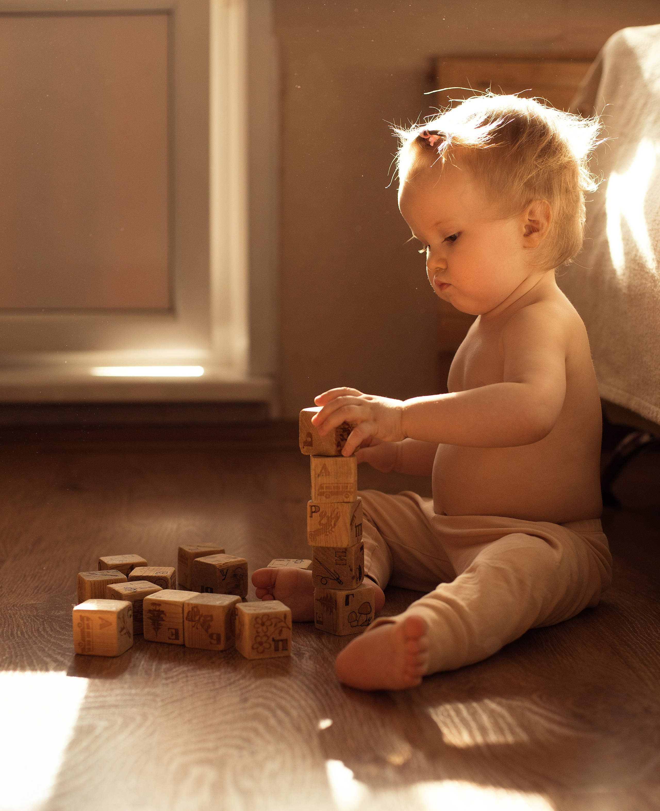 Девочка с голым торсом играет с деревянными кубиками в лучах солнечного света