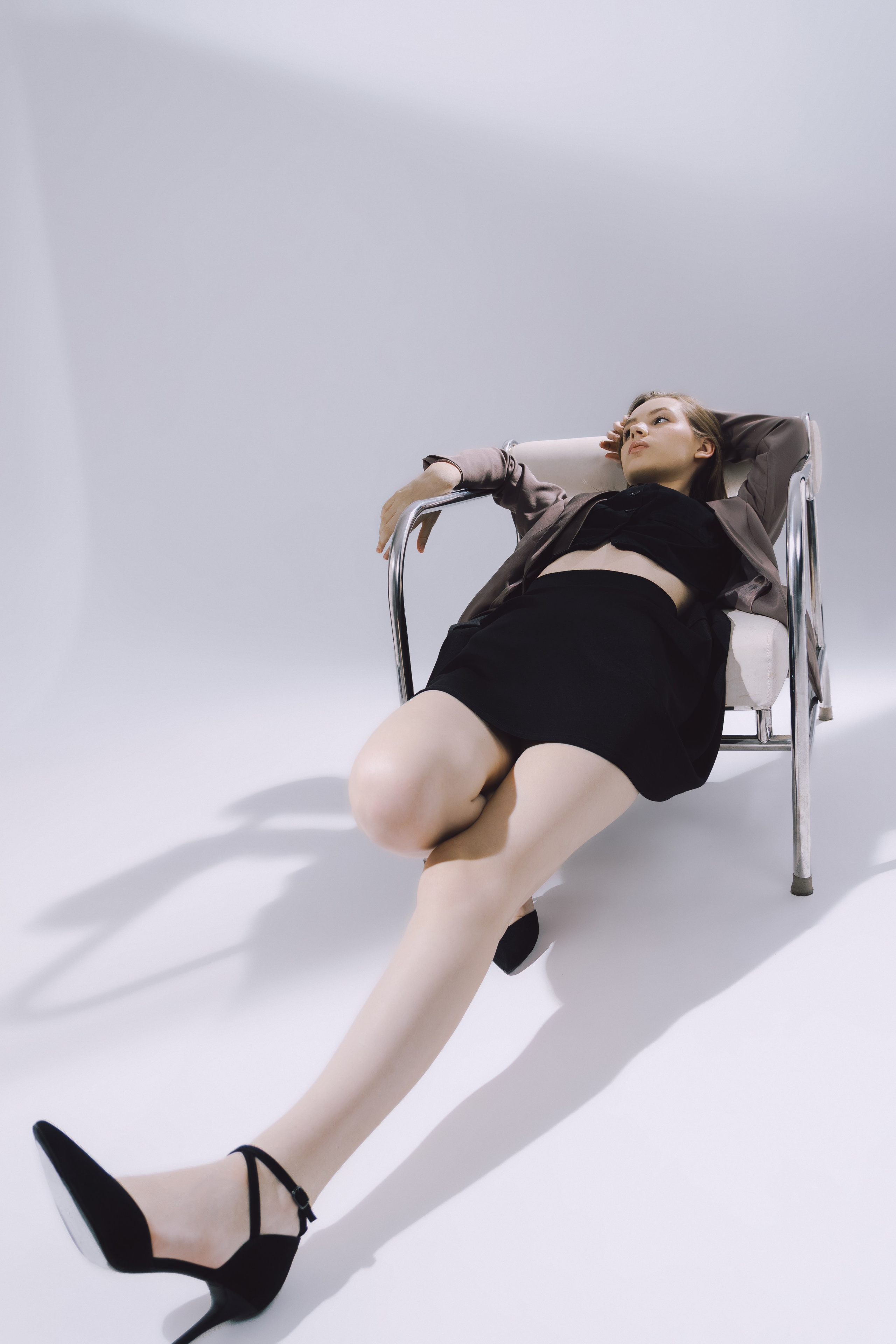 Чёрное платье, пиджак и туфли на каблуке: гармония стиля на фоне студийного минимализма.