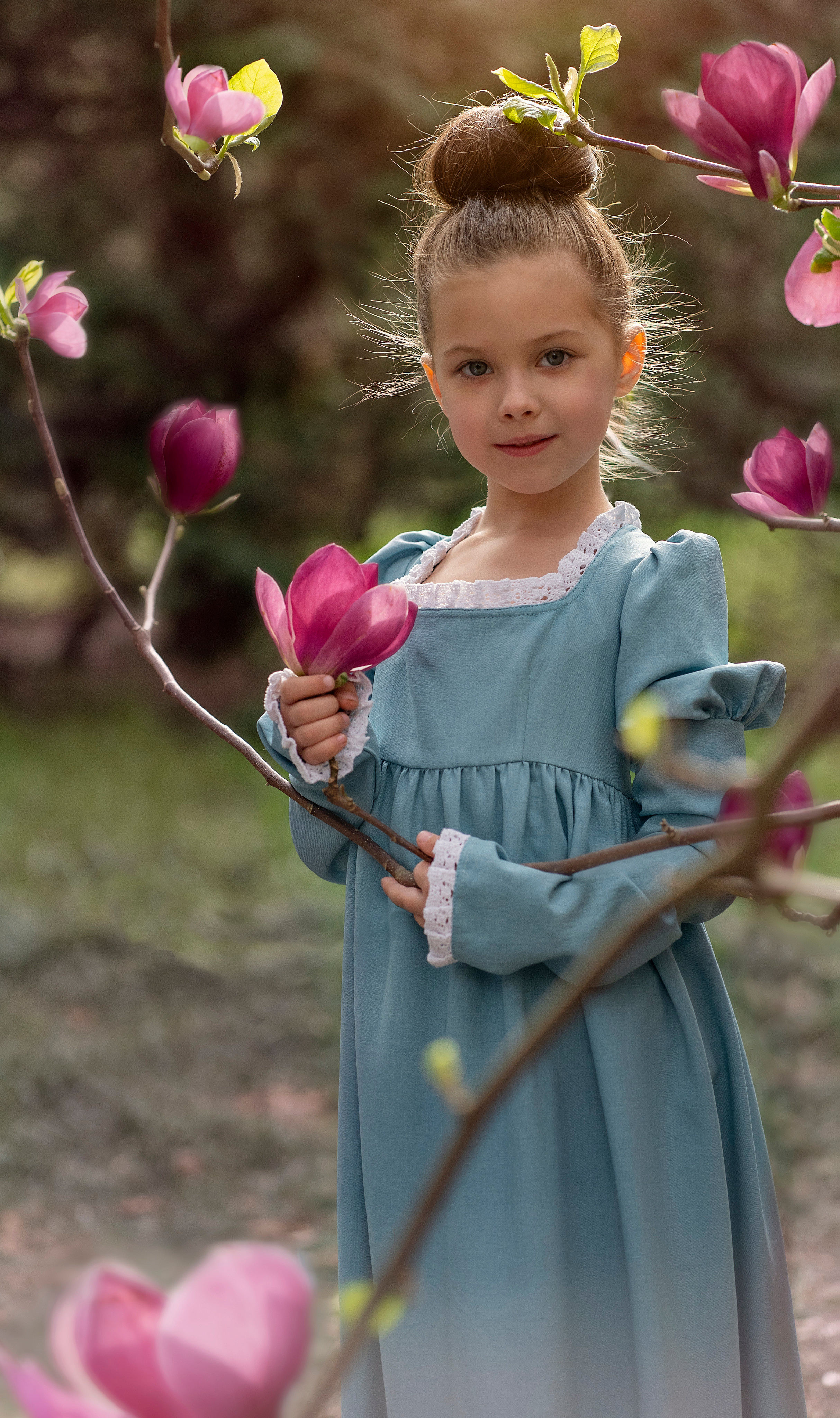 Девочка, по имени-Амелия, в парке фотографируется на фоне магнолии.