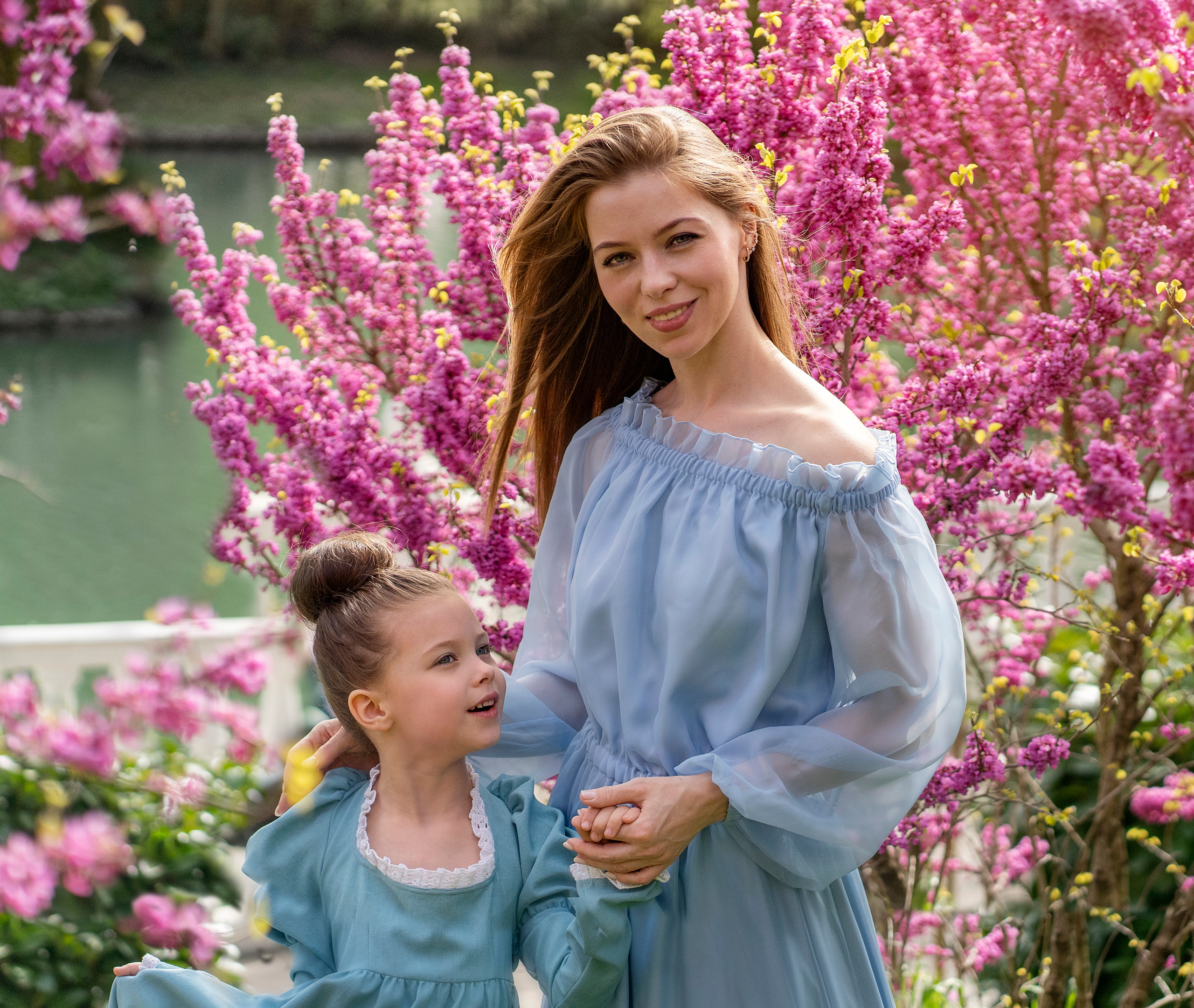 Мама с дочкой, фотографируются на фоне цветущего дерева.