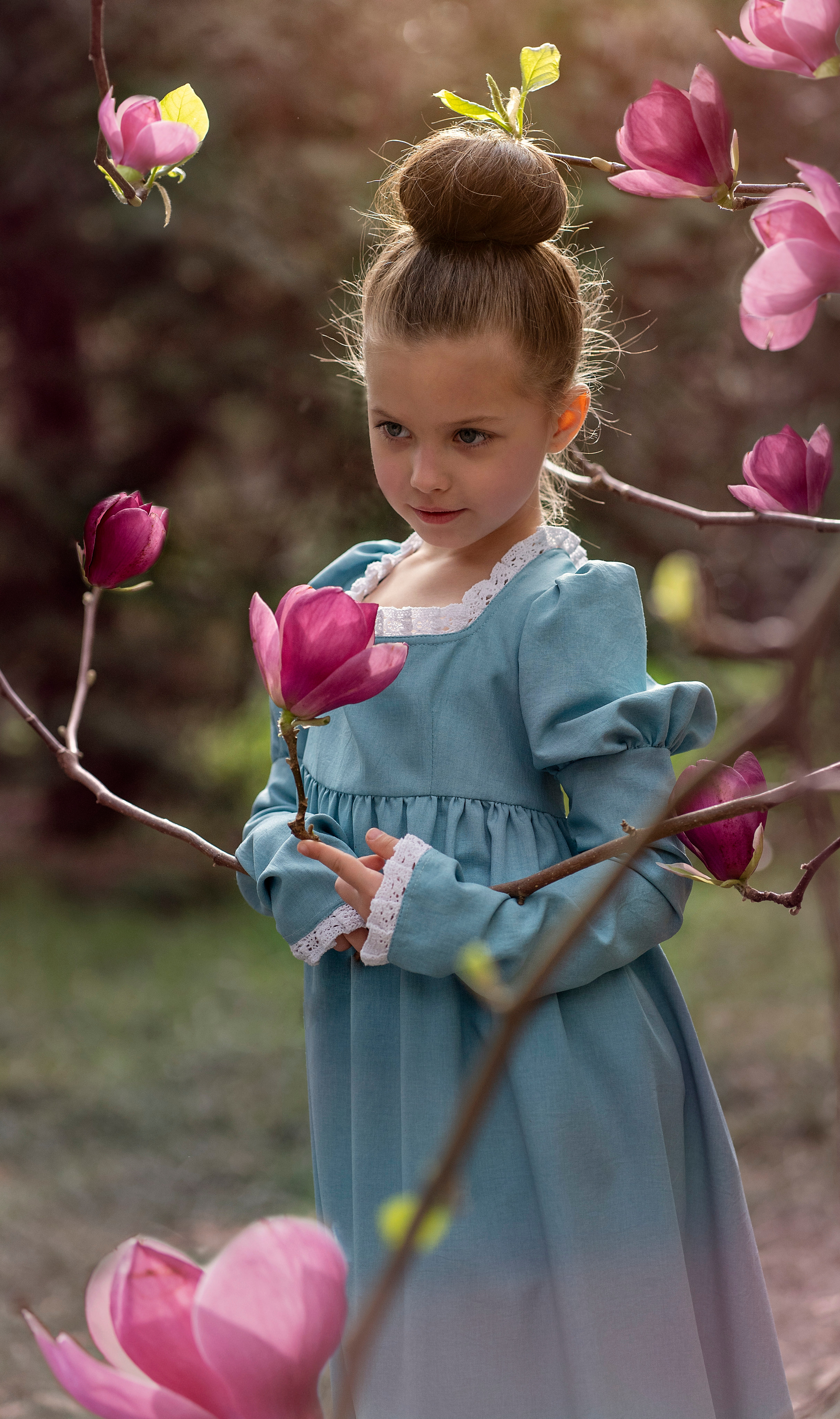 Маленькая девочка любуется цветущей магнолией. 