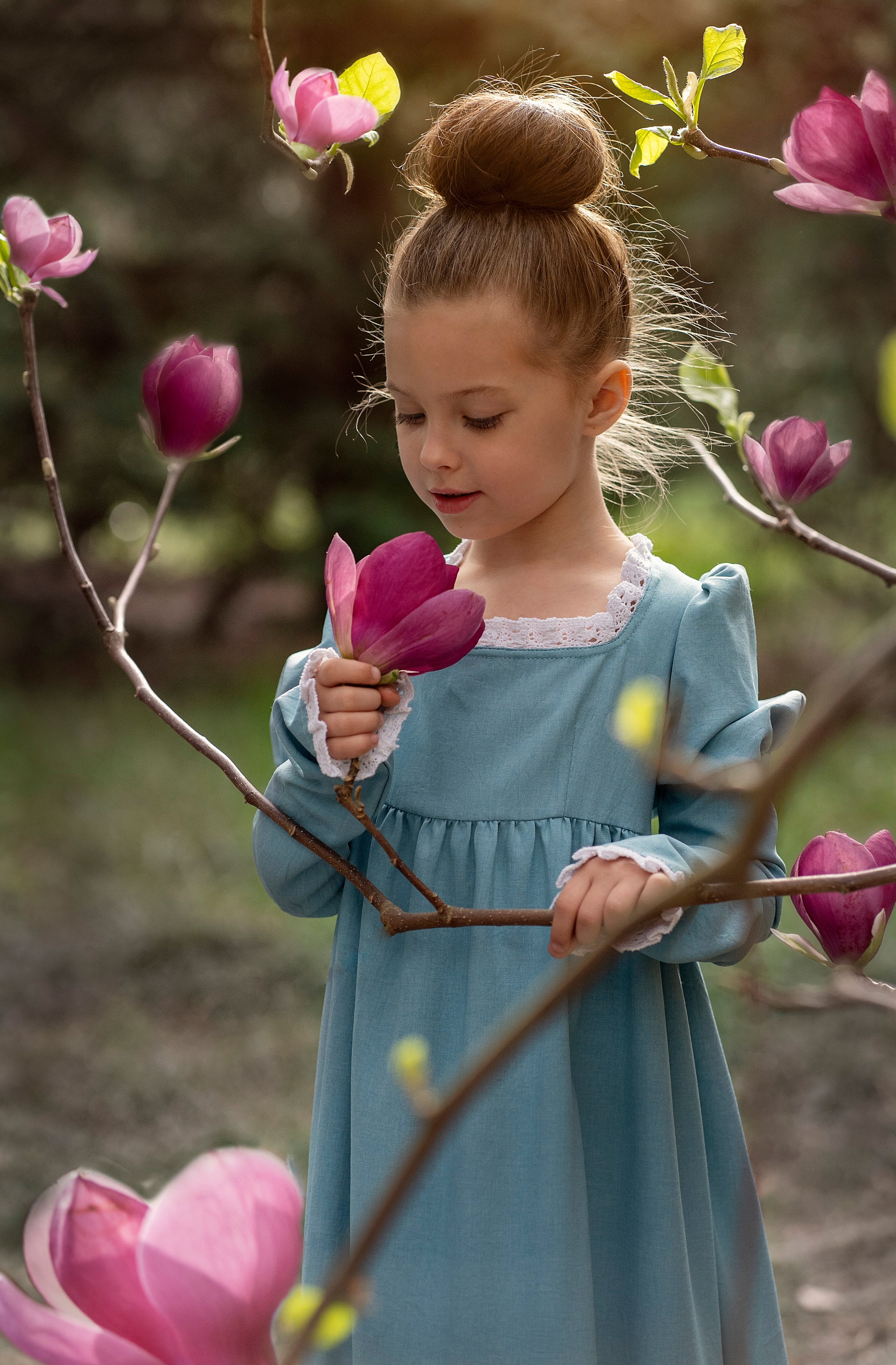Девочка в старинном платье нюхает магнолию.