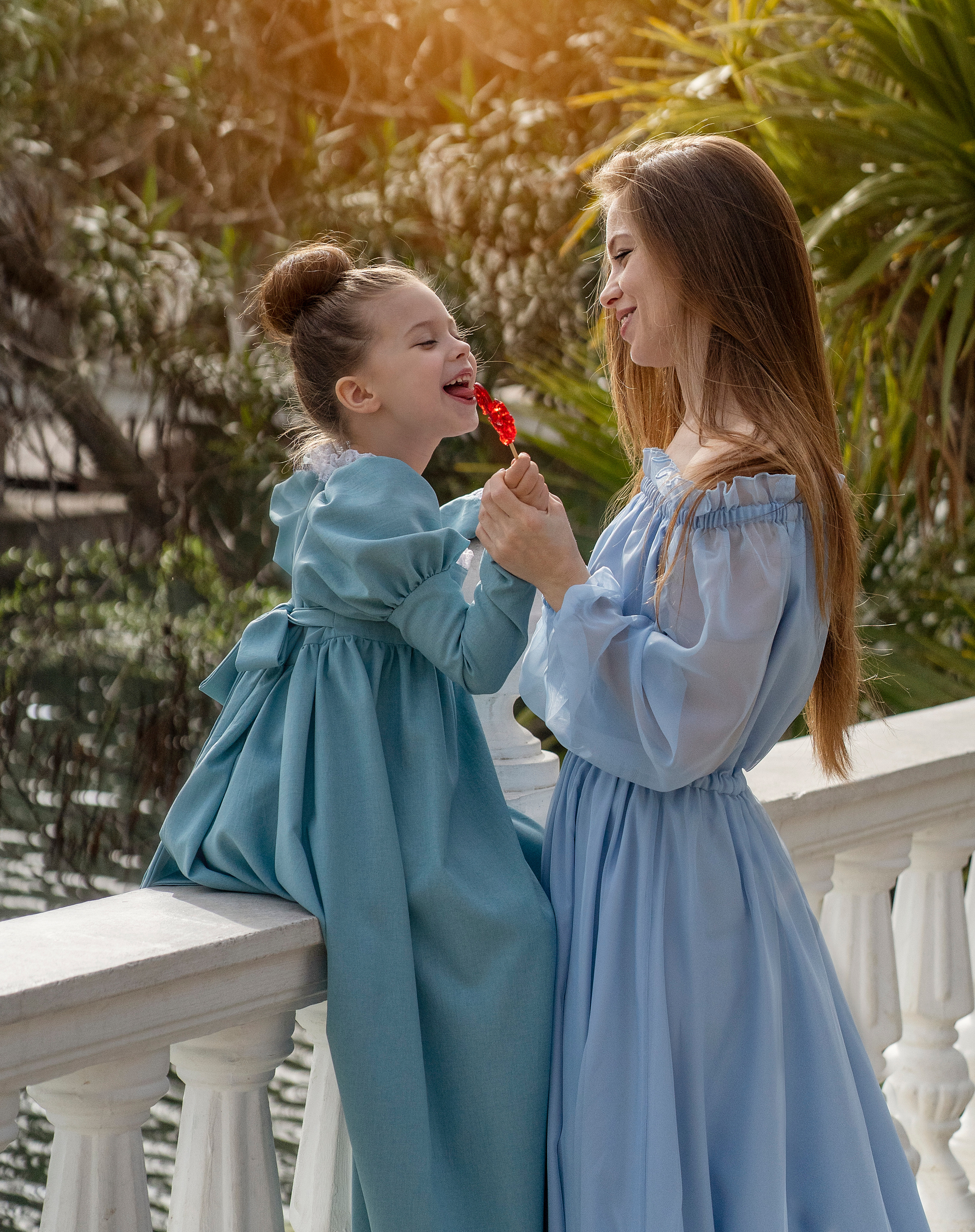 Дочка украдкой от мамы слизывает петушка на палочке.