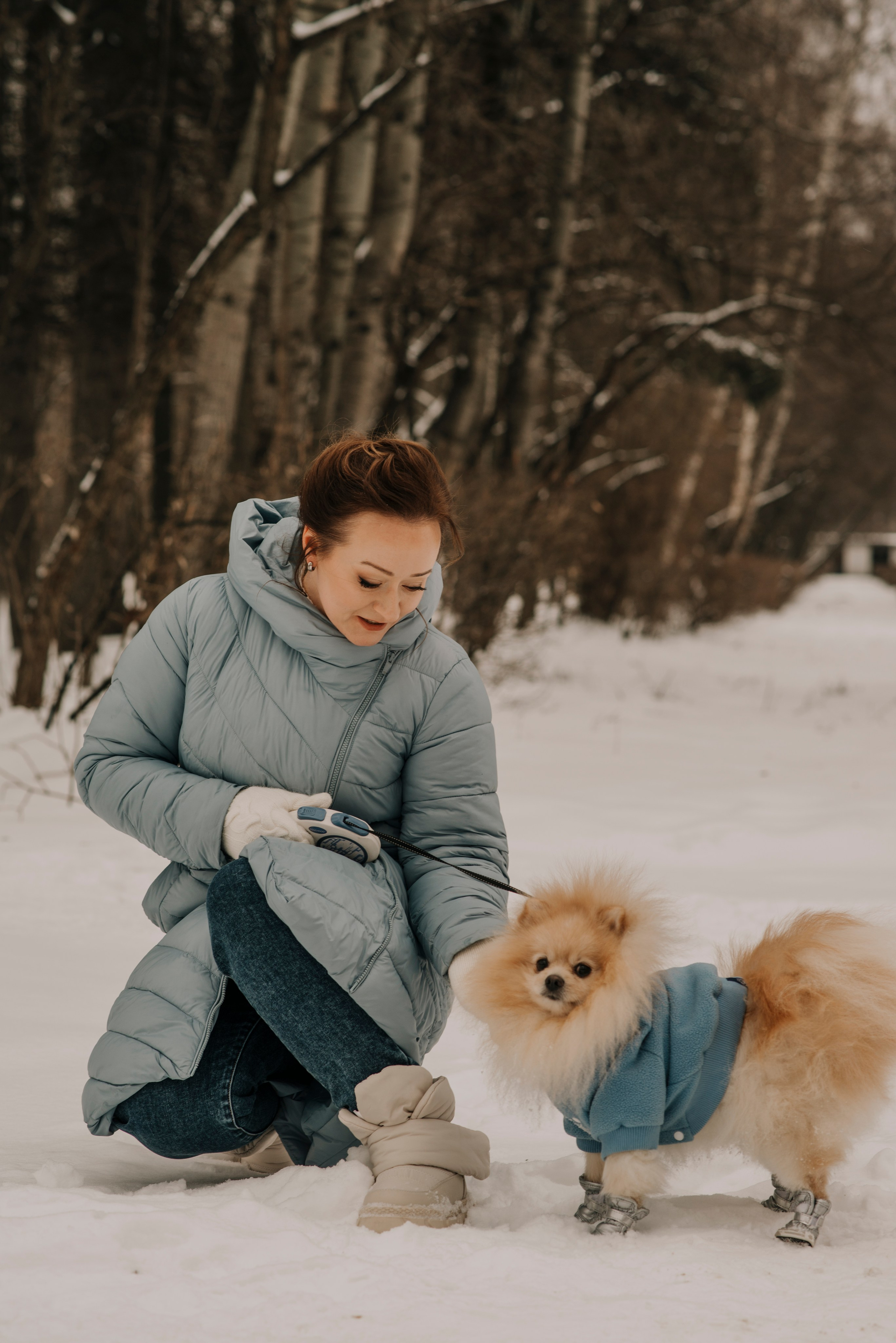 Зимняя фотосессия рыжеволосой девушки на фоне снега в лесу с собакой шпицем