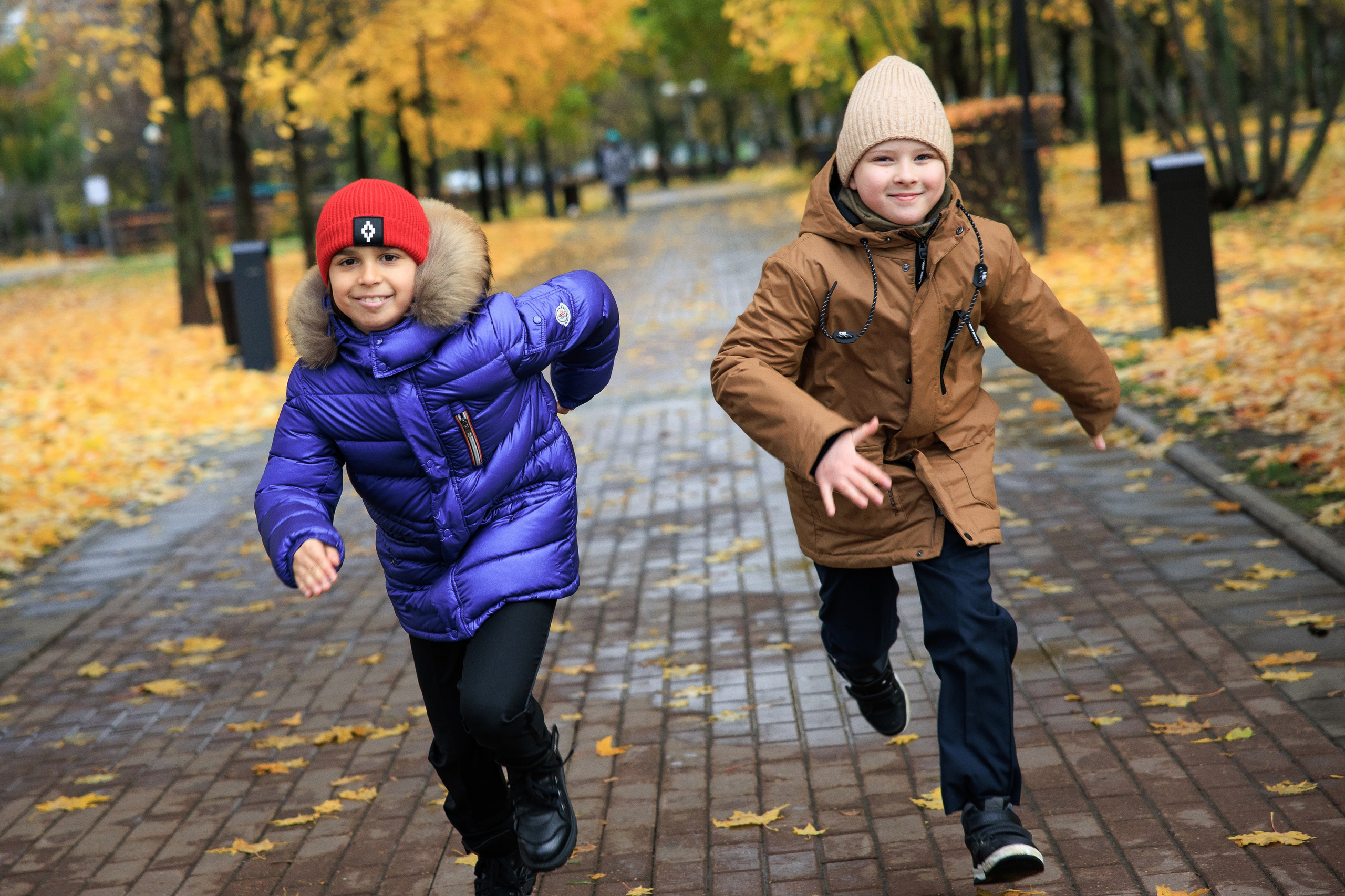 Два мальчика бегут по осенней дорожке в парке