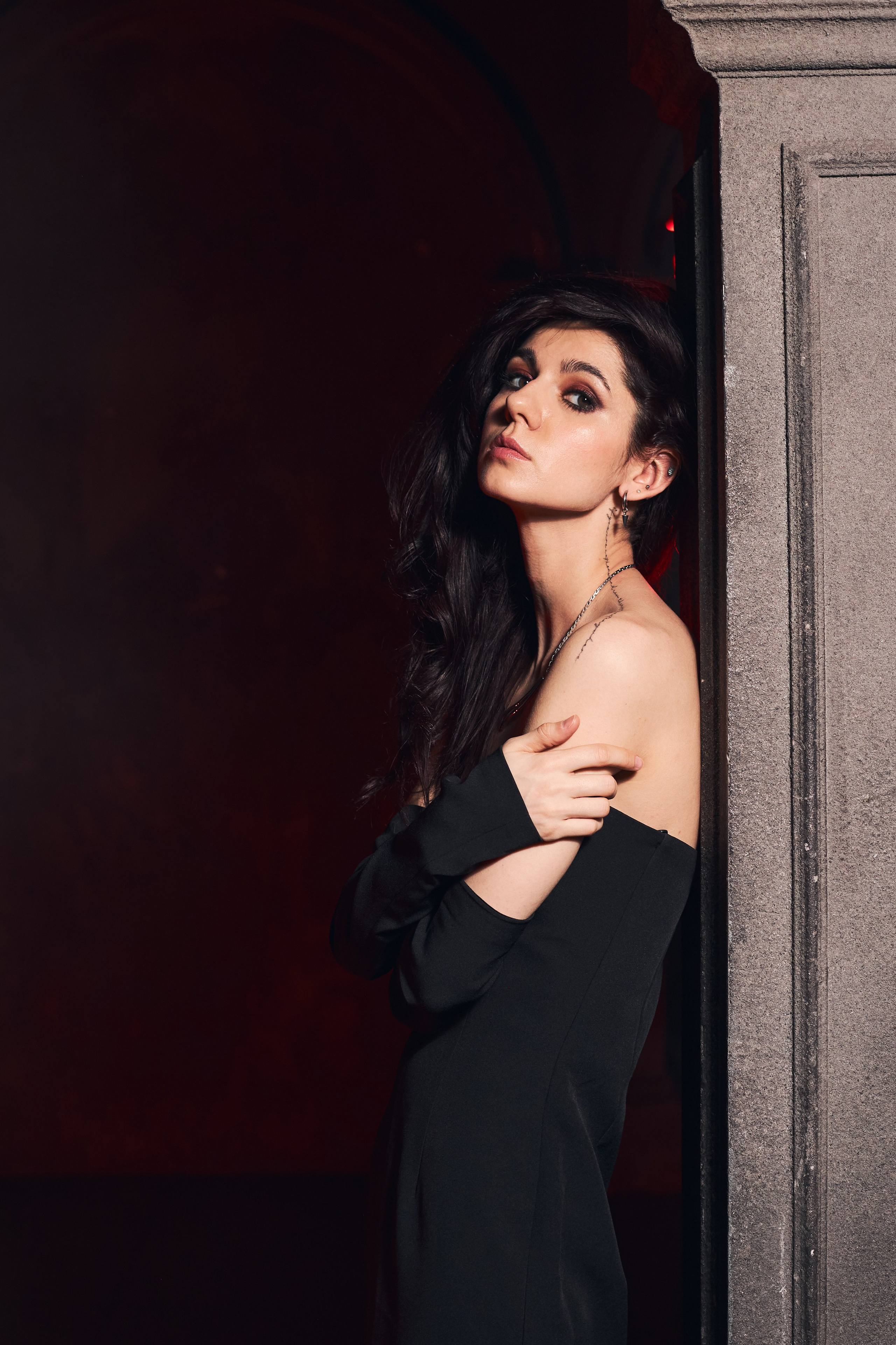 Портрет девушки в открытом платье, которая стоит у готической колонны, прислонившись к ней спиной и обхватив себя за плечи