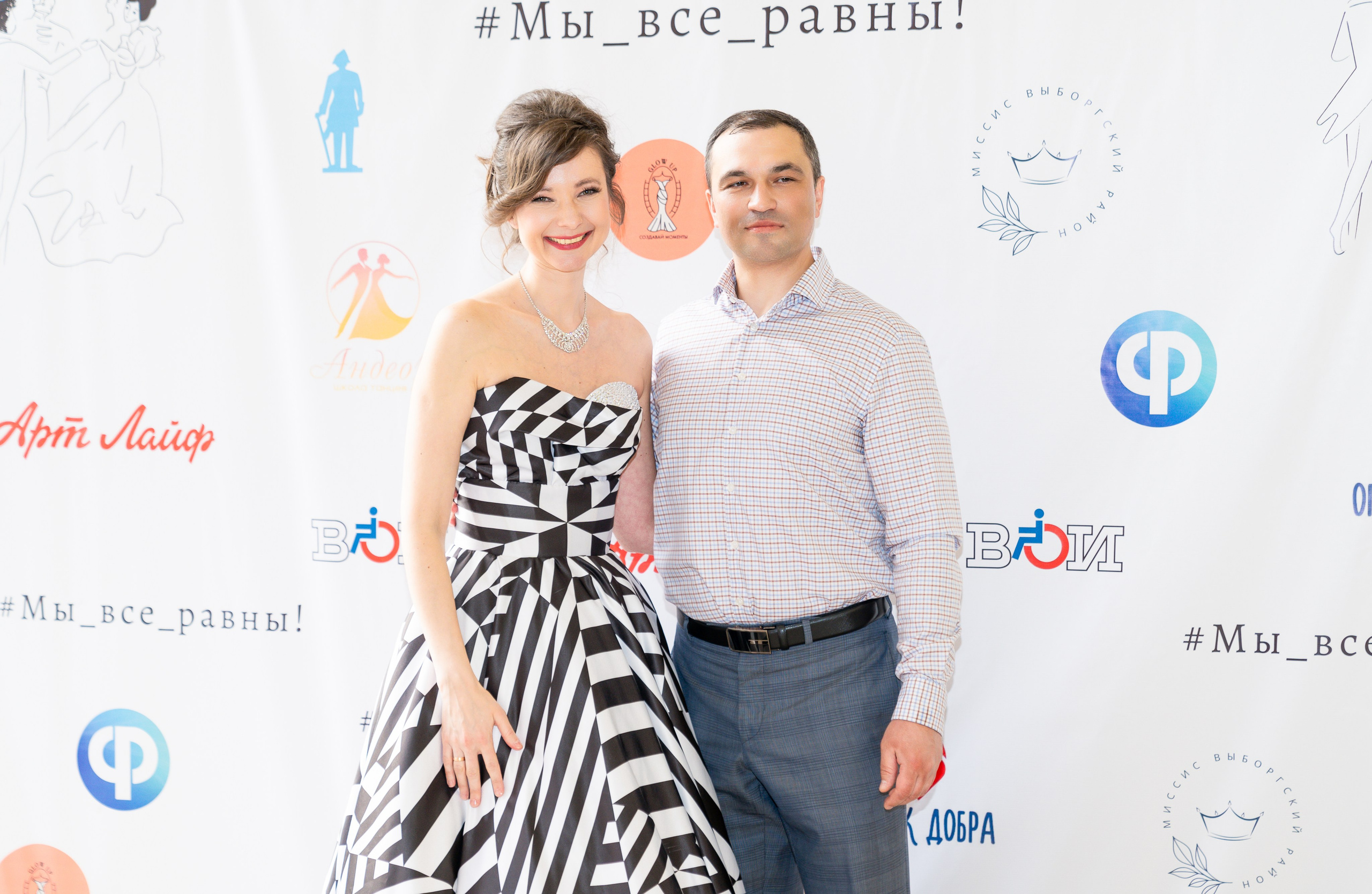 Пара на инклюзивном балу «Мы все равны»: женщина в чёрно-белом платье и мужчина в клетчатой рубашке позируют у баннера. Фотограф Мальцев Евгений.