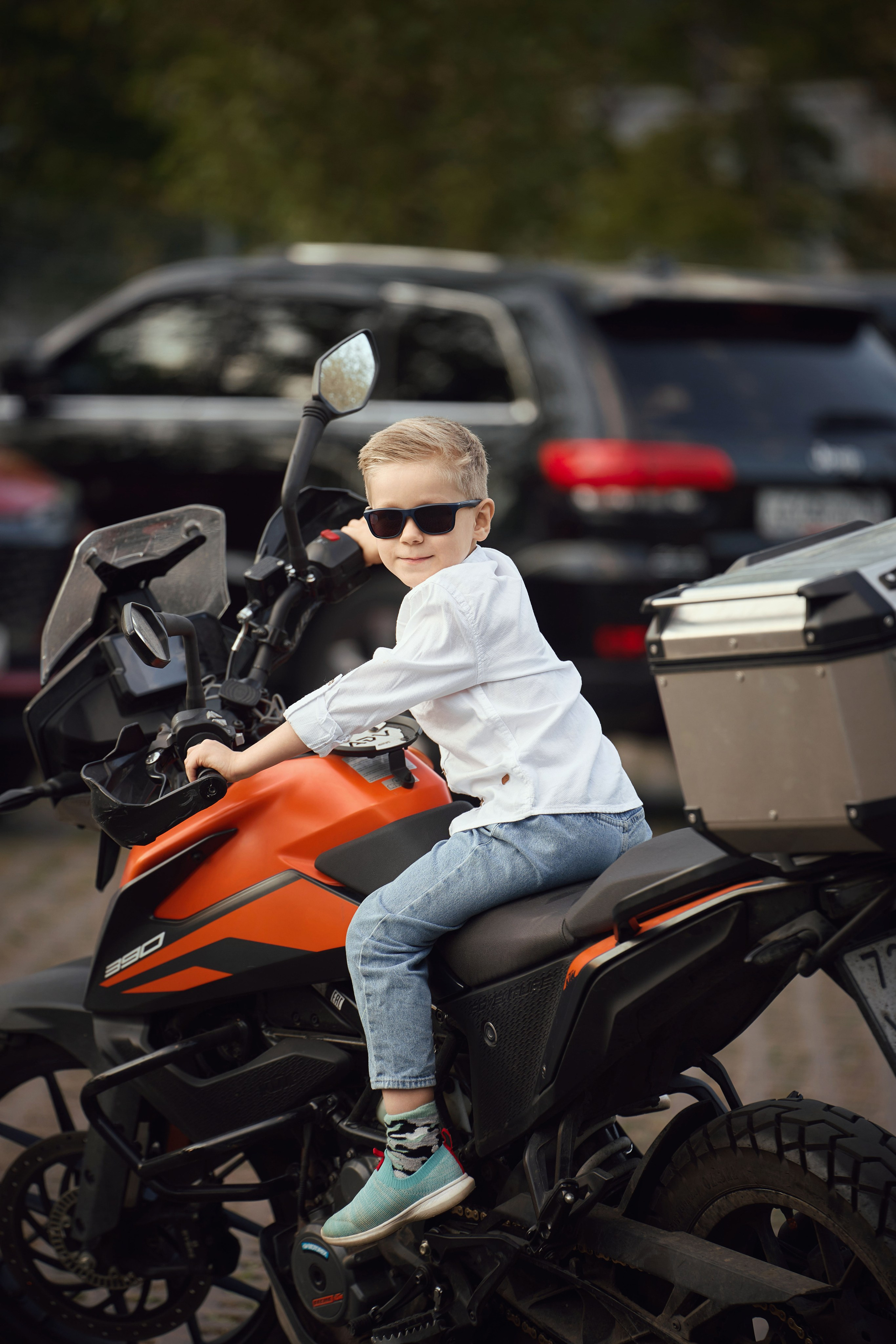 мальчик в белой рубашке и голубых джинсах и солнцезащитных очках сидит на оранжевом мотоцикле ктм 390 на ВДНХ 
