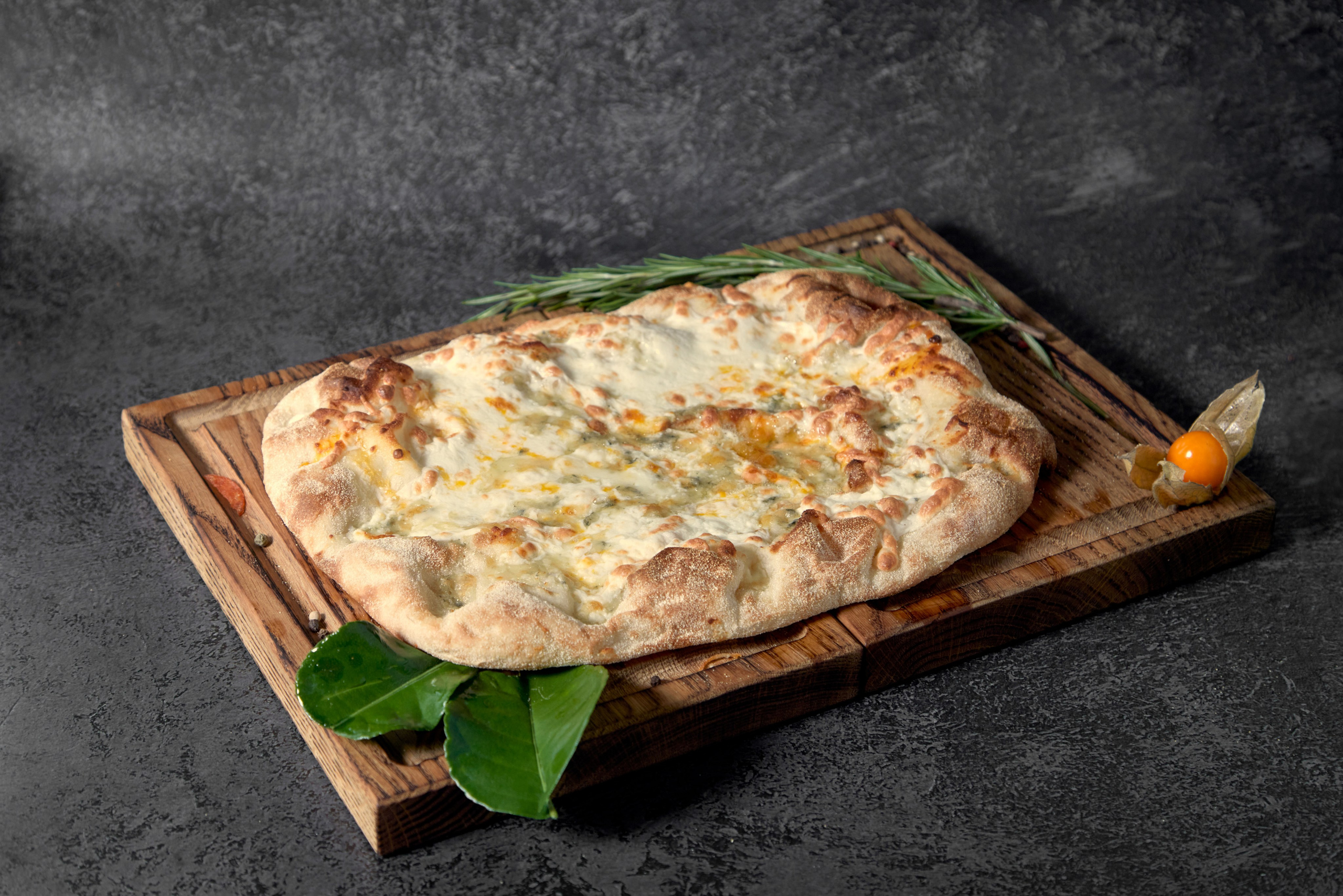 Пицца с сыром и зеленью на деревянной доске.