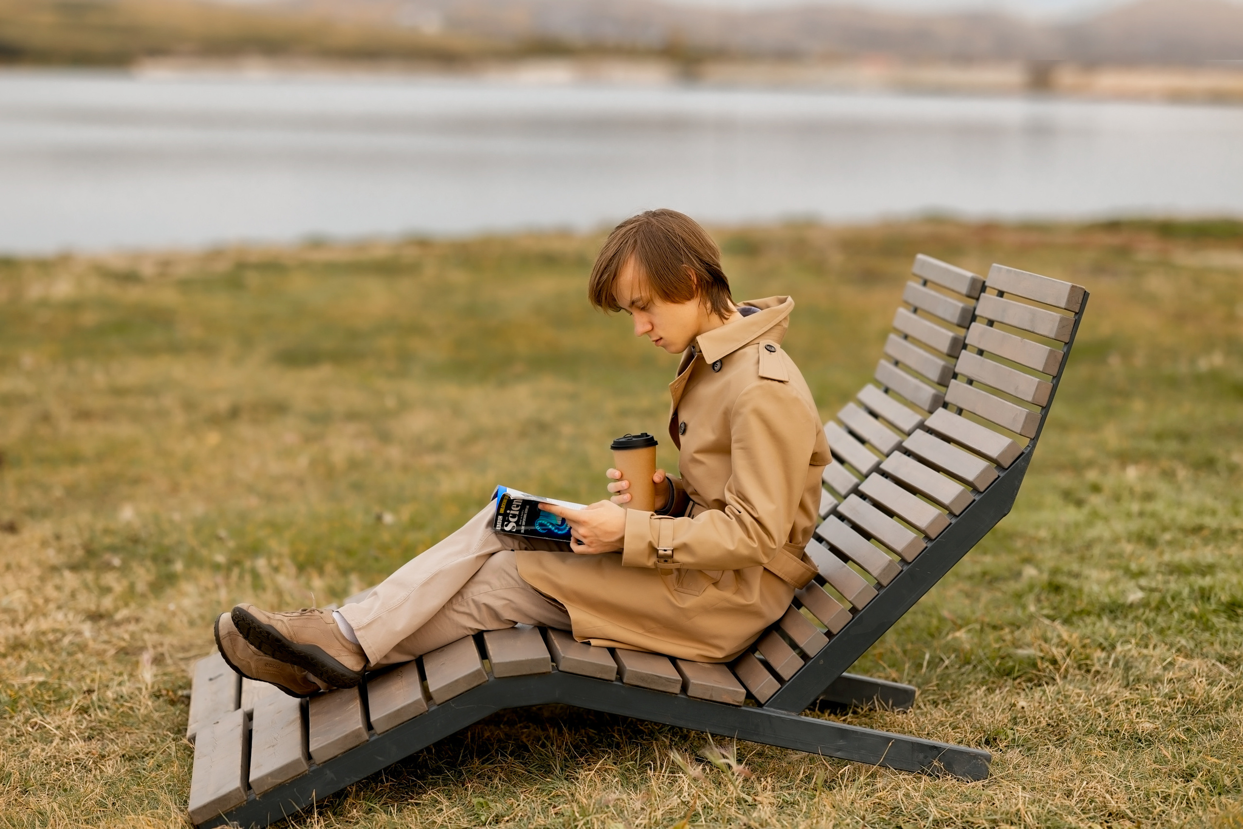 Мужчина в шезлонге возле осеннего озера читает газету