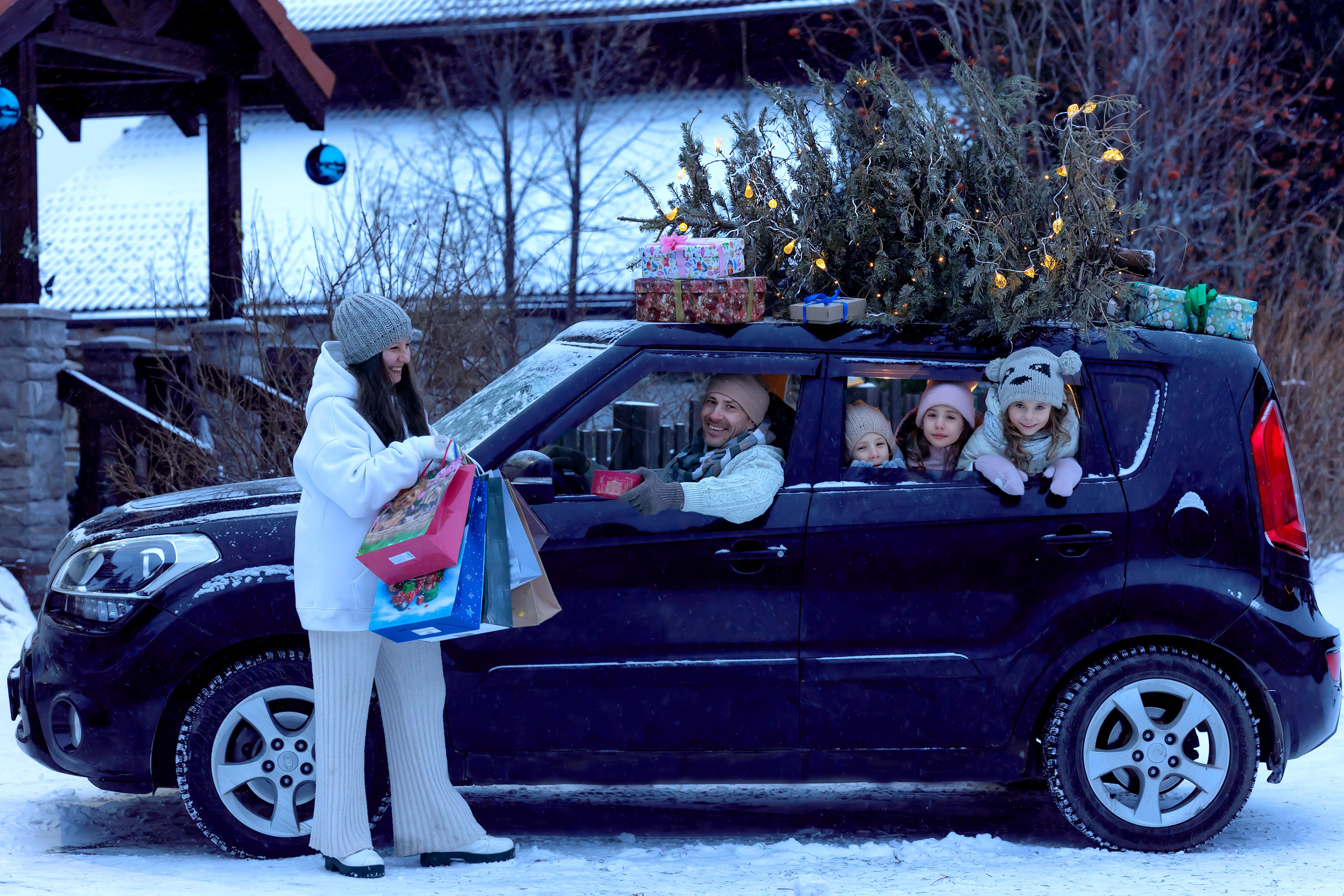 Новогодняя машина с ёлкой на крыше. Счастливая семья в машине дарит подарки