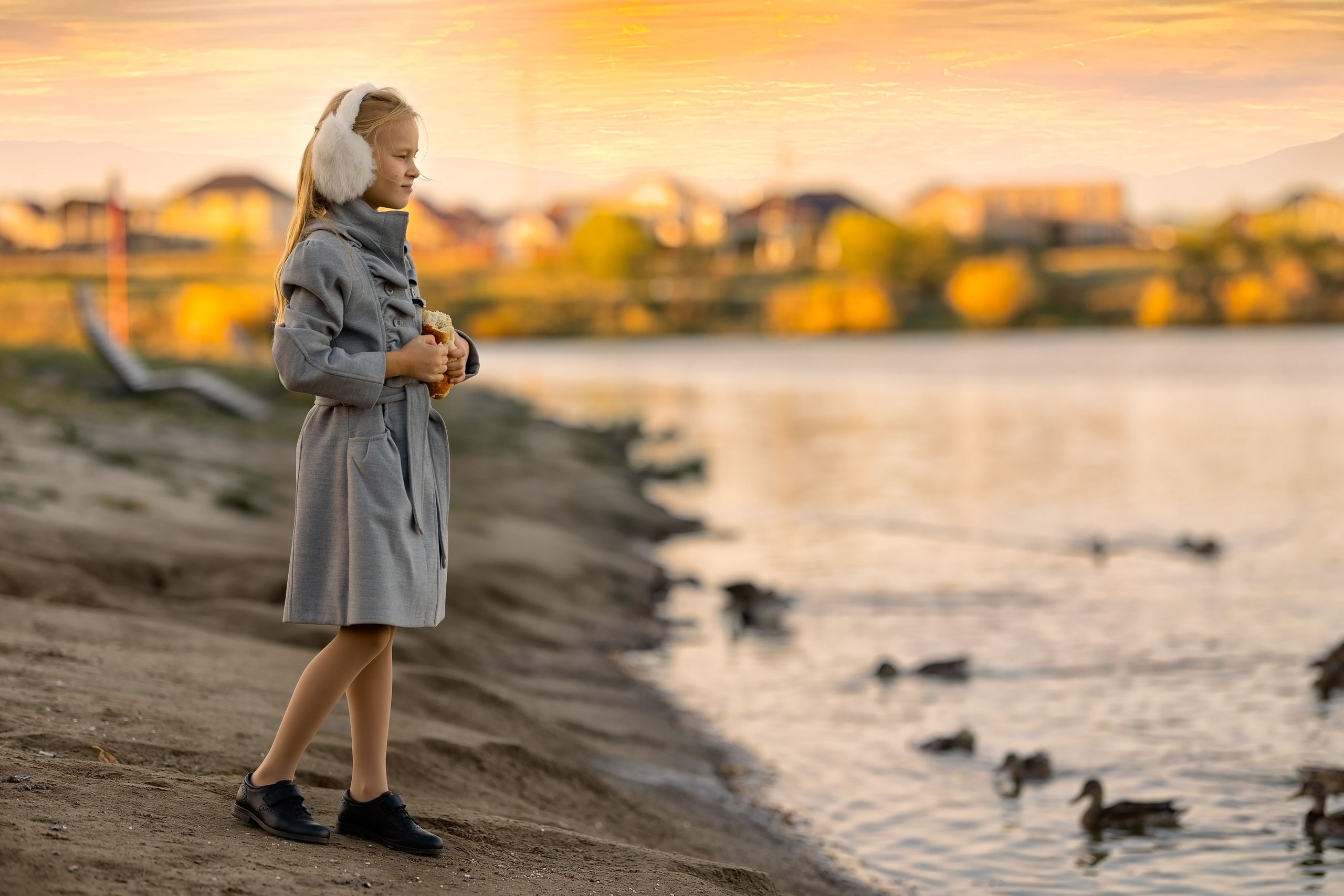 Осенний парк. Возле озера девочка кормит уток. 