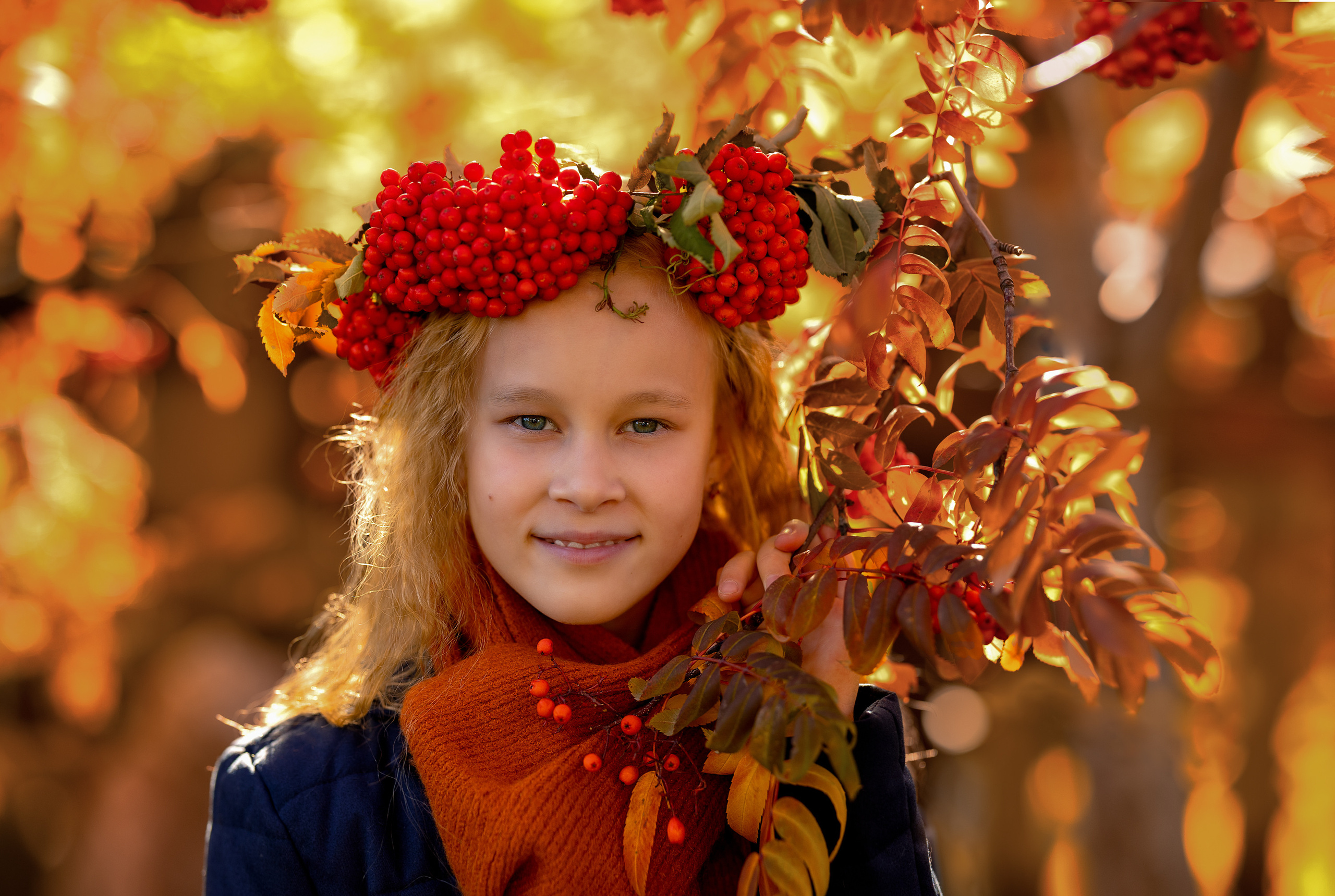 Девочка возле багряной рябины осенью в венке из ягод
