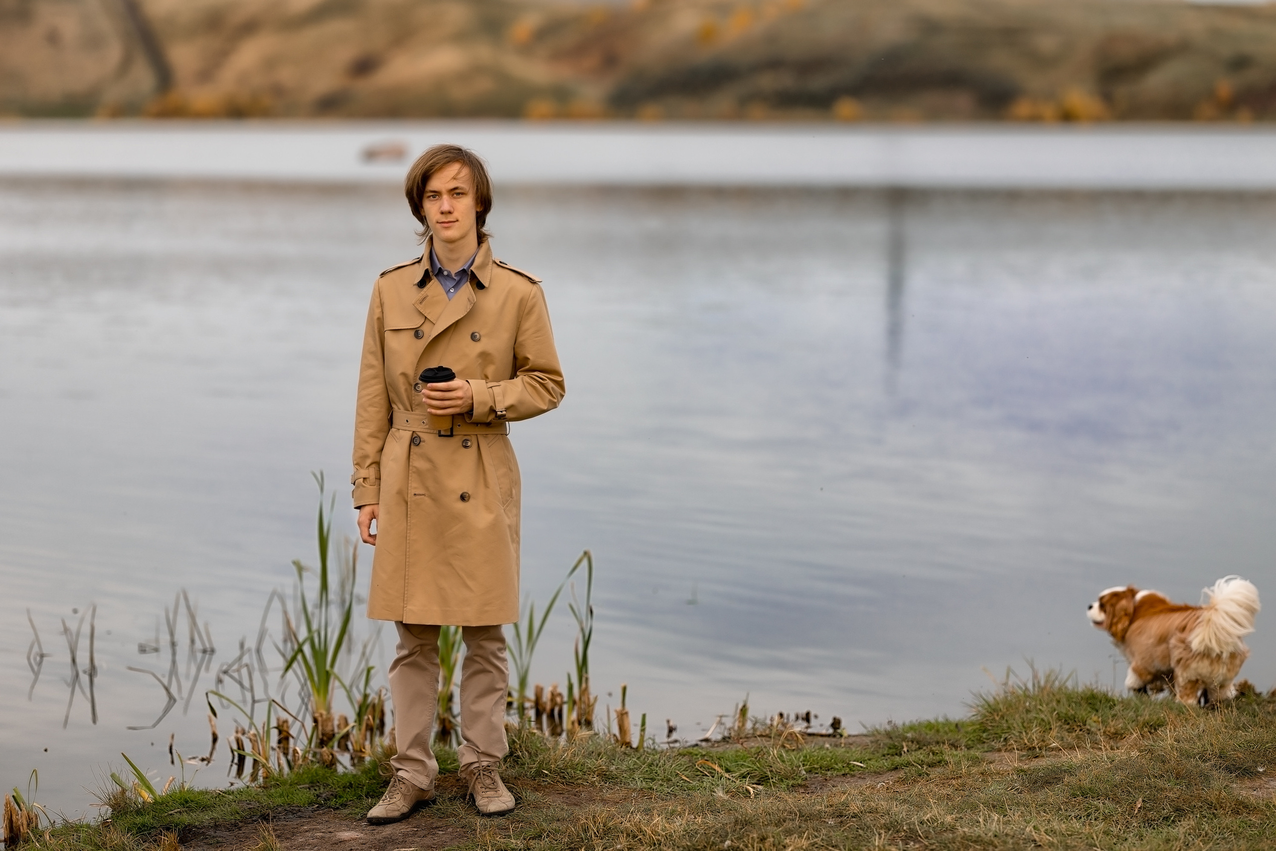 Мужчина возле озера осенью пьет кофе