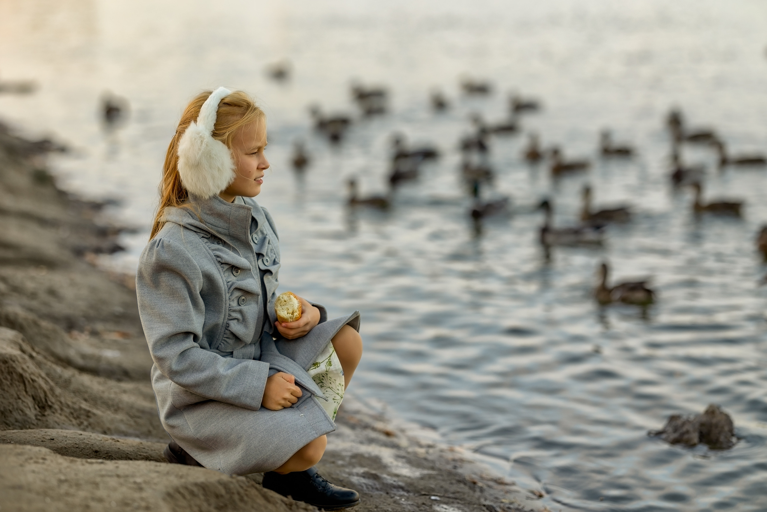 Девочка осенью возле озера с собакой кормит уточек