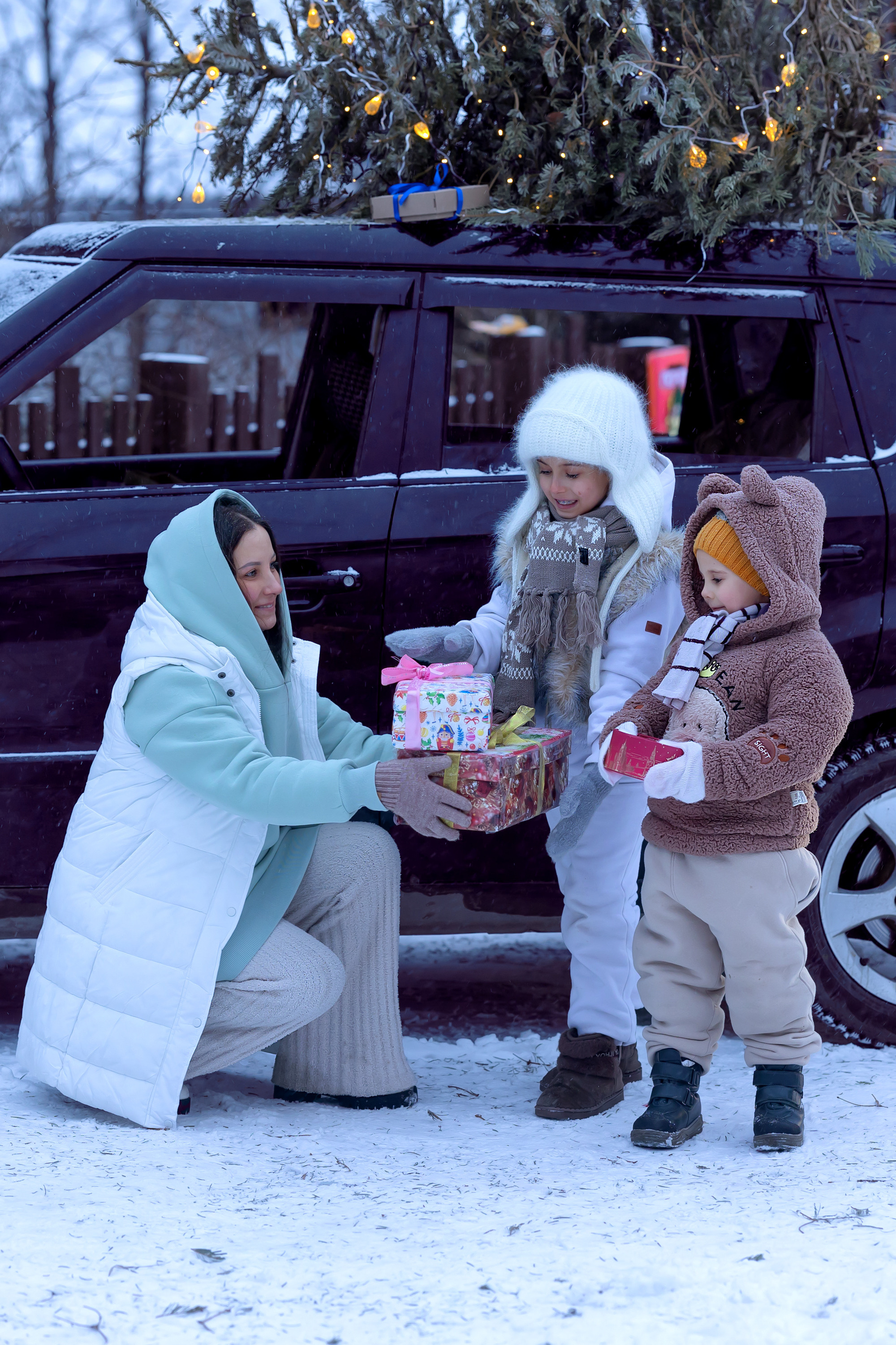 Новогодняя машина с ёлкой на крыше. Счастливая семья в машине дарит подарки