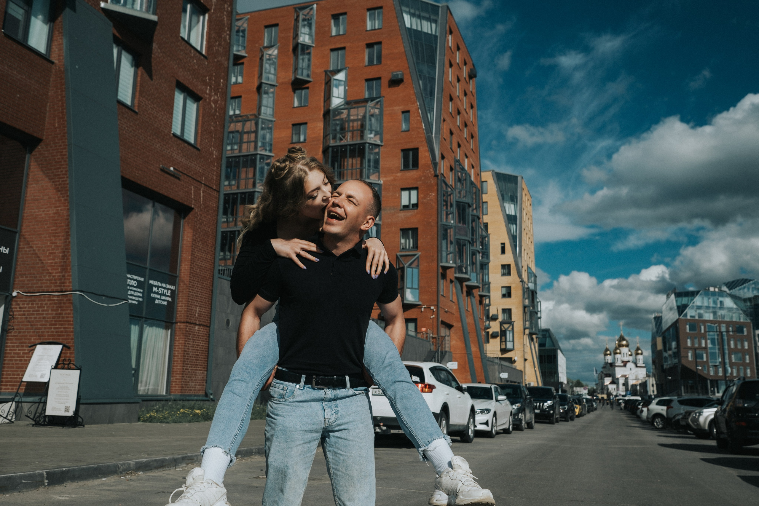 Молодая пара мужчина и девушка дурачатся в городских локациях в черных футболках и синих джинсах, лав стори для влюбленной пары на кануне свадьбы