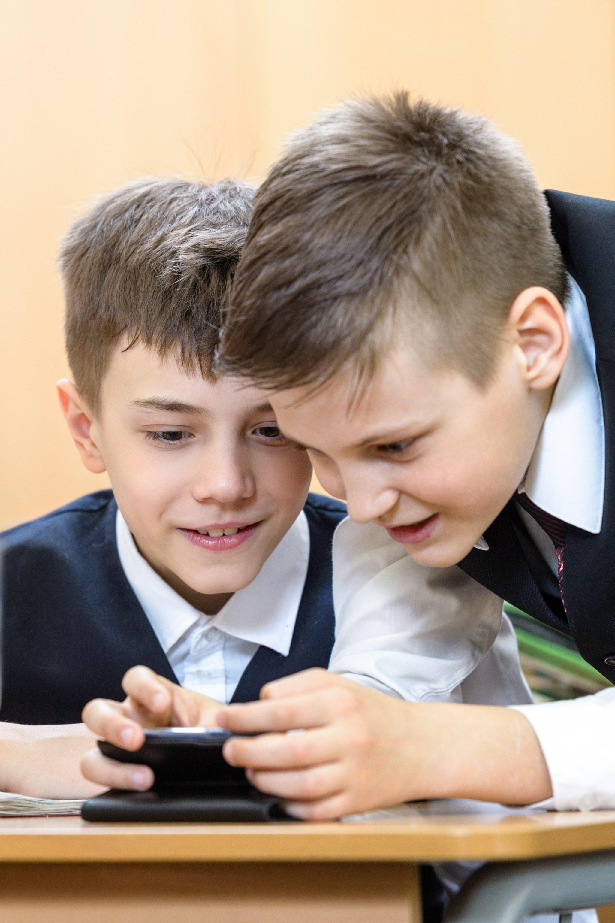 Два школьника увлечённо смотрят в смартфон на перемене