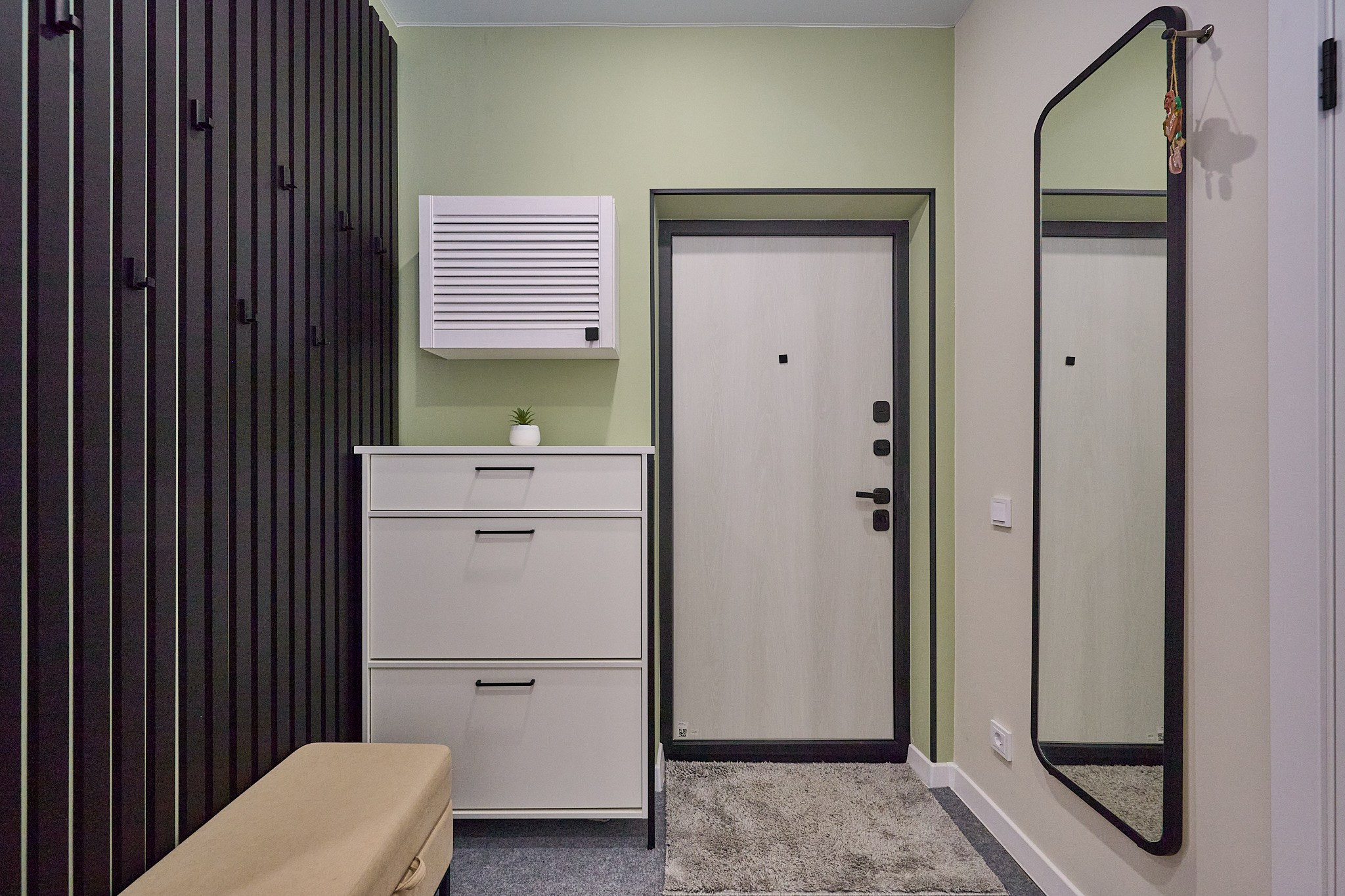 коридор белая тумба белая дверь большое зеркало черная деревянная вешалка на стене бежевый пуфик 