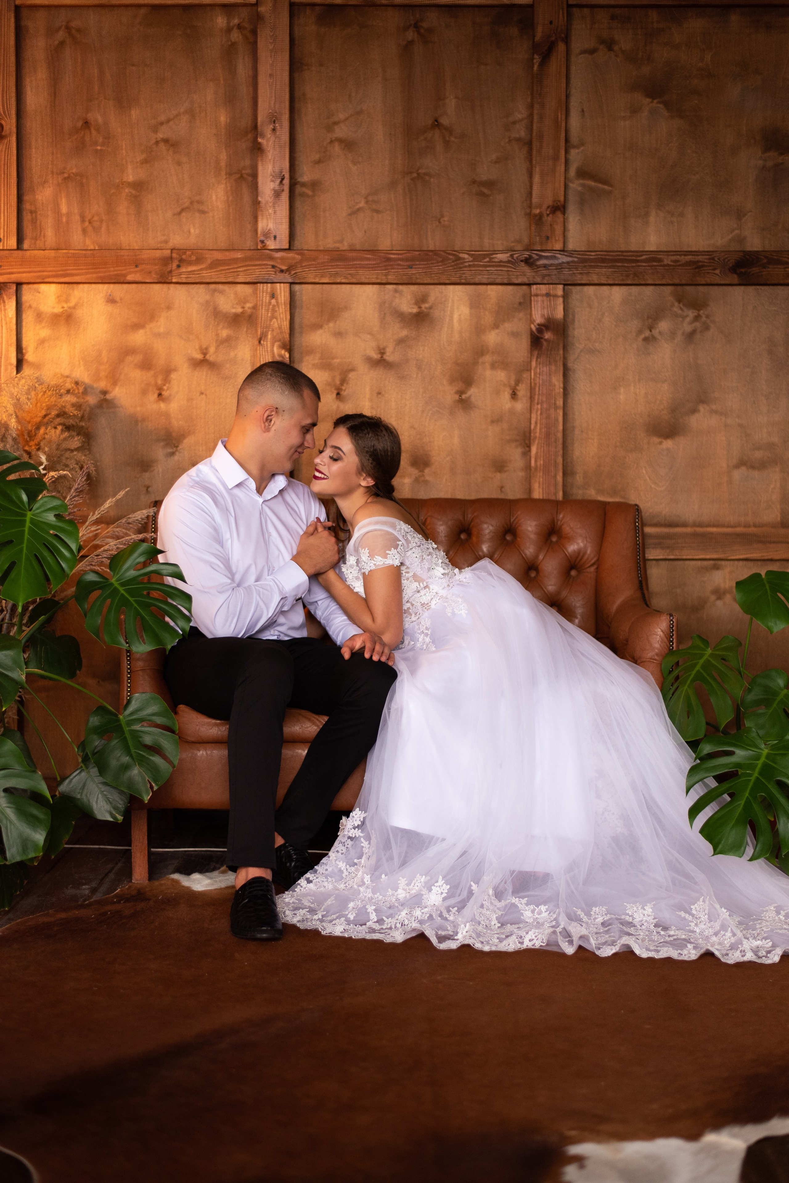Жених и невеста в затемненной студии на кожаном диване в Краснодаре