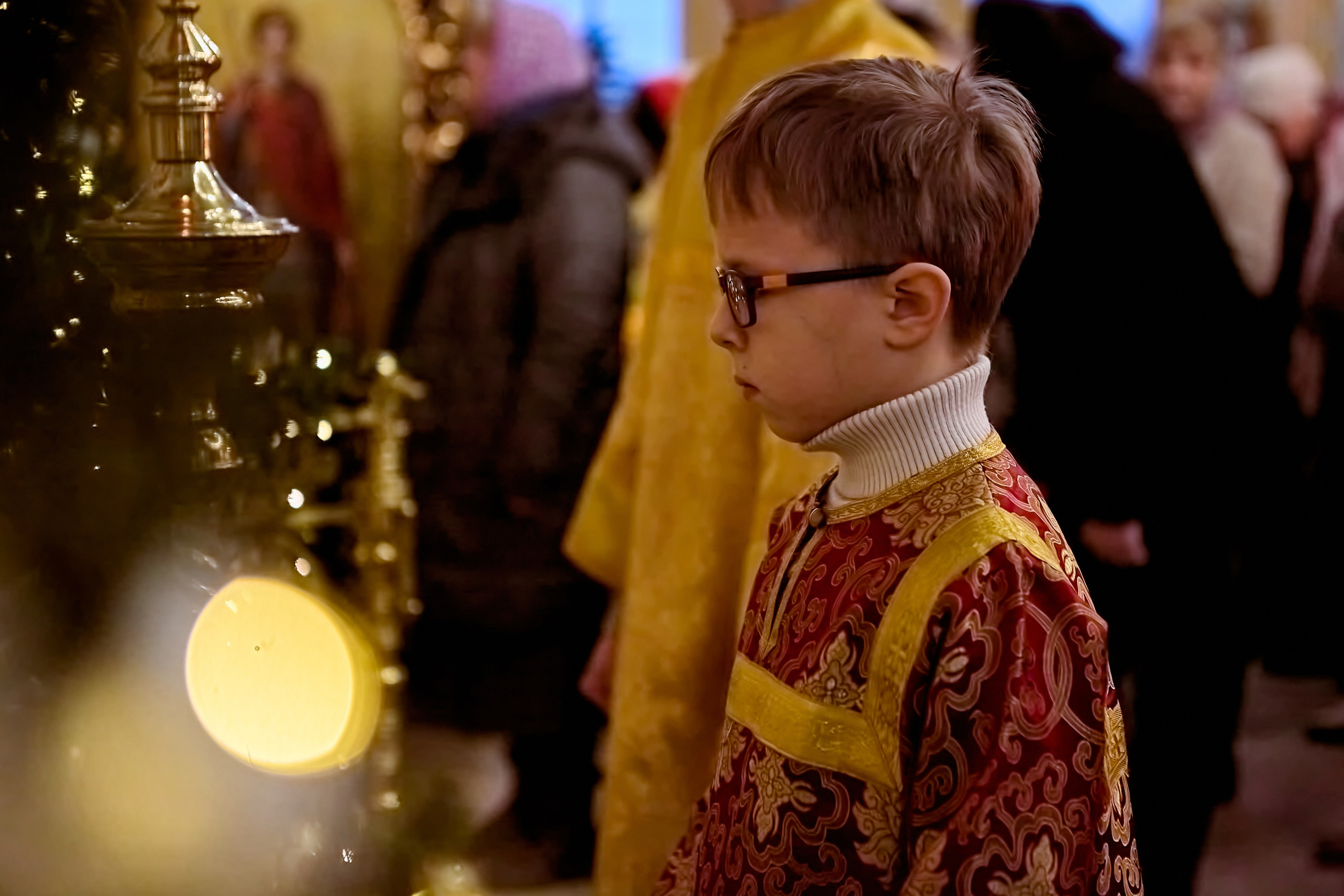 Мальчик 8 лет в красно-бордовом стихаре пред амвоном со свечой