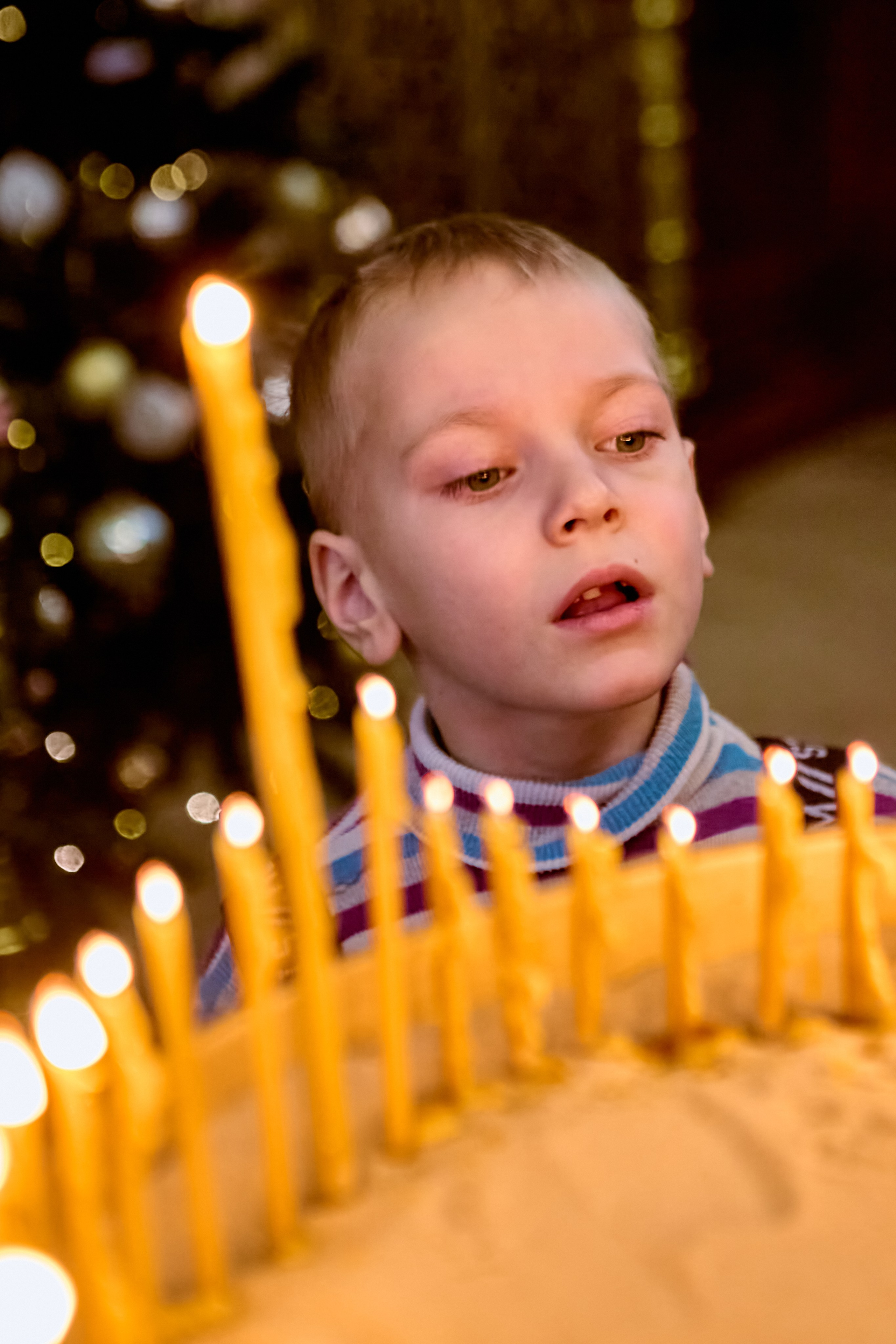 Мальчик 4-6 лет с удивлением заглядывает в подсвечник где горят свечи