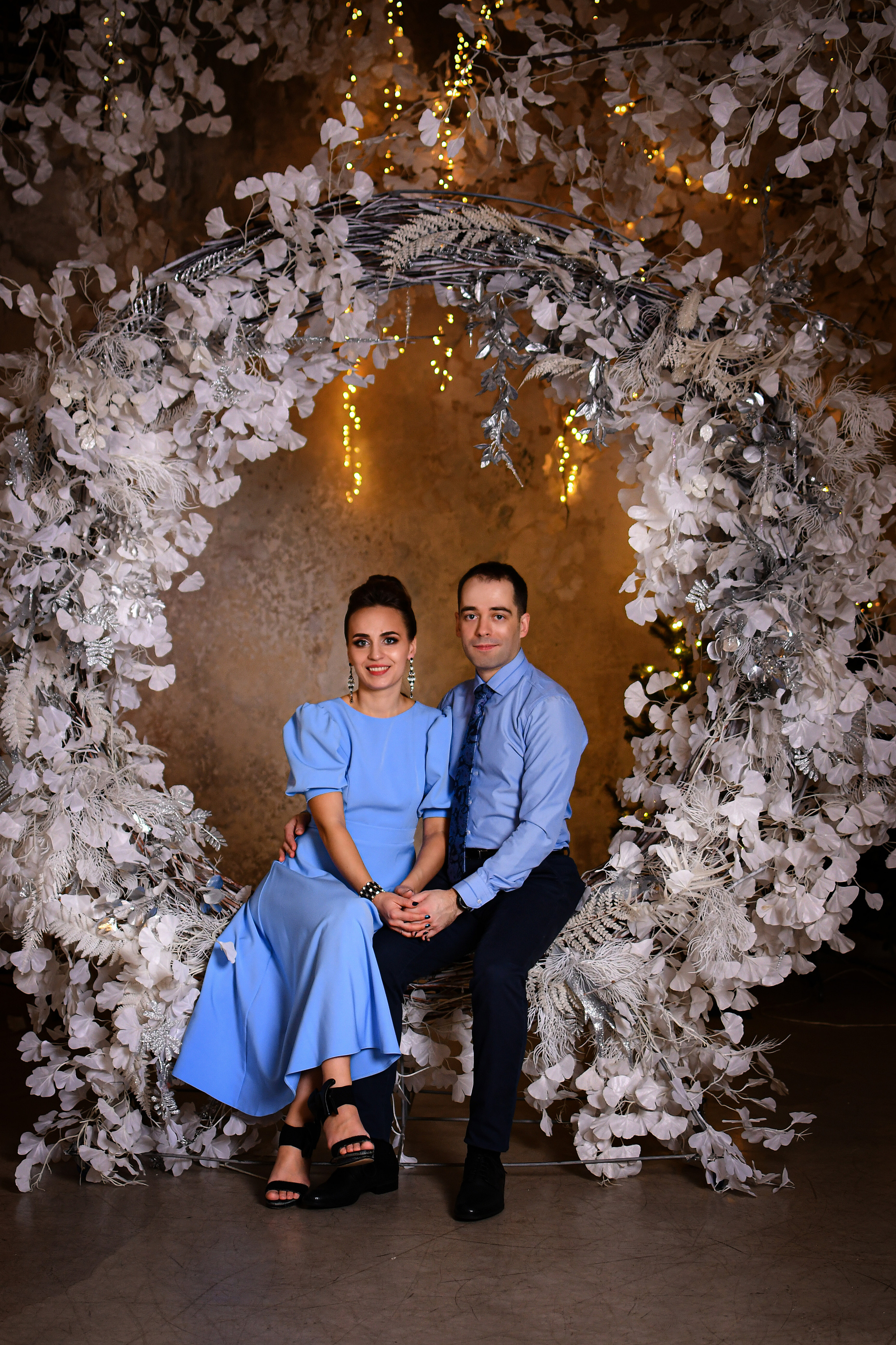 Красивая пара сидит перед аркой цветов в фотостудии Павильон Спб