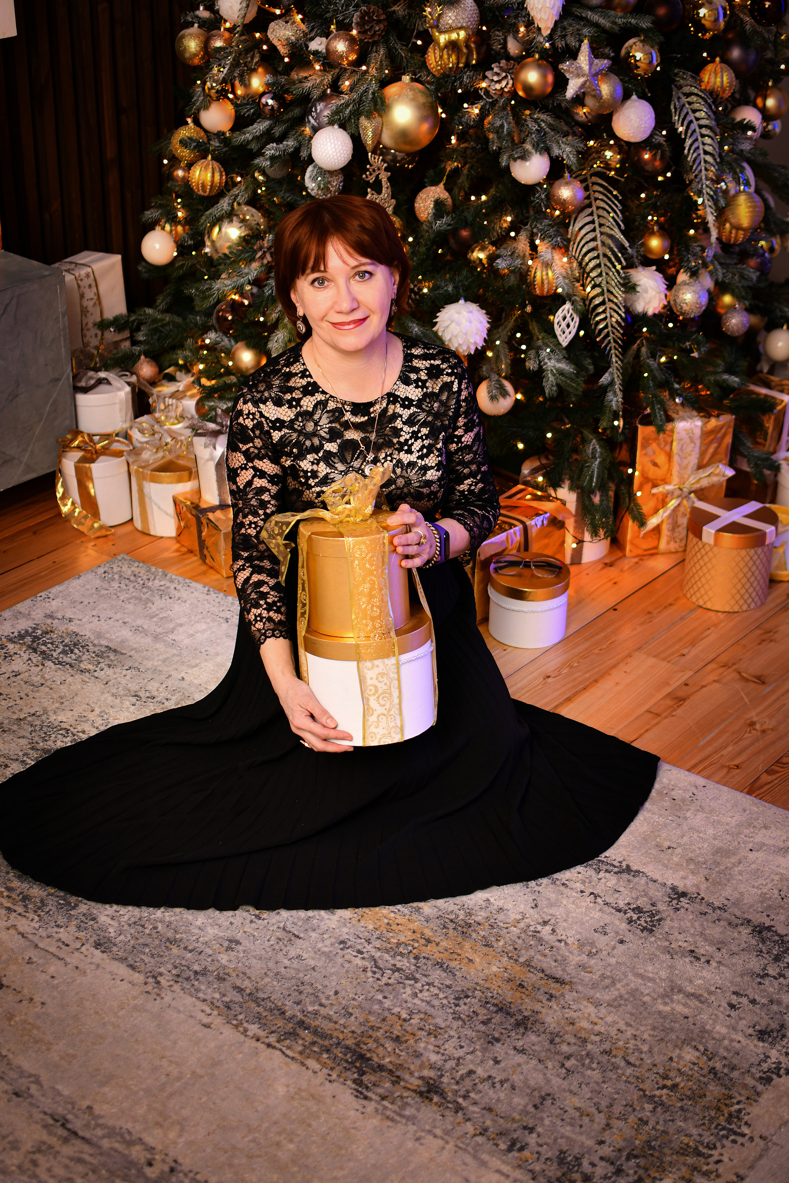 Женщина в вечернем платье сидит у елки с подарком