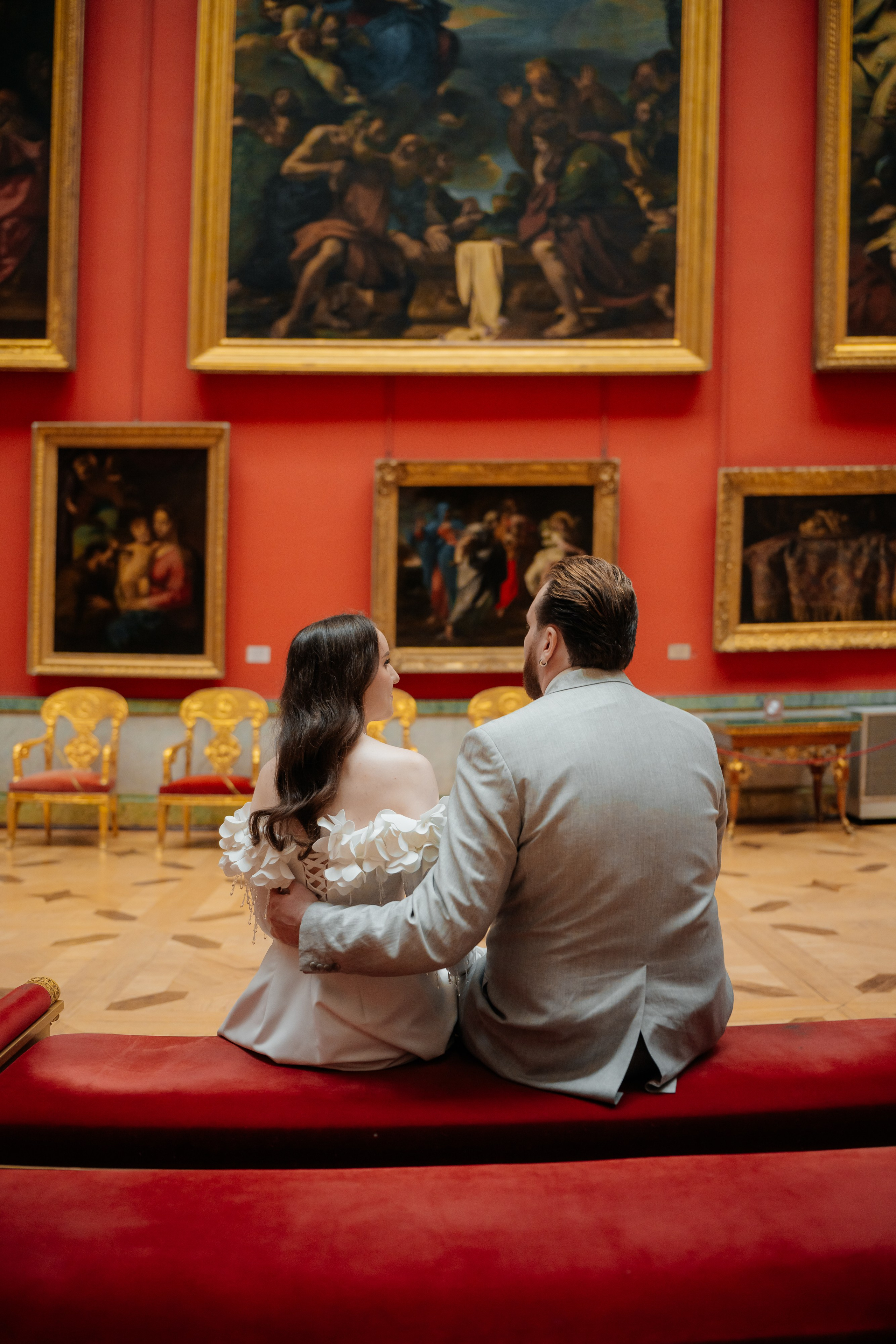 Свадебная фотосессия в Эрмитаже жених и невеста сидят на диване в красном зале