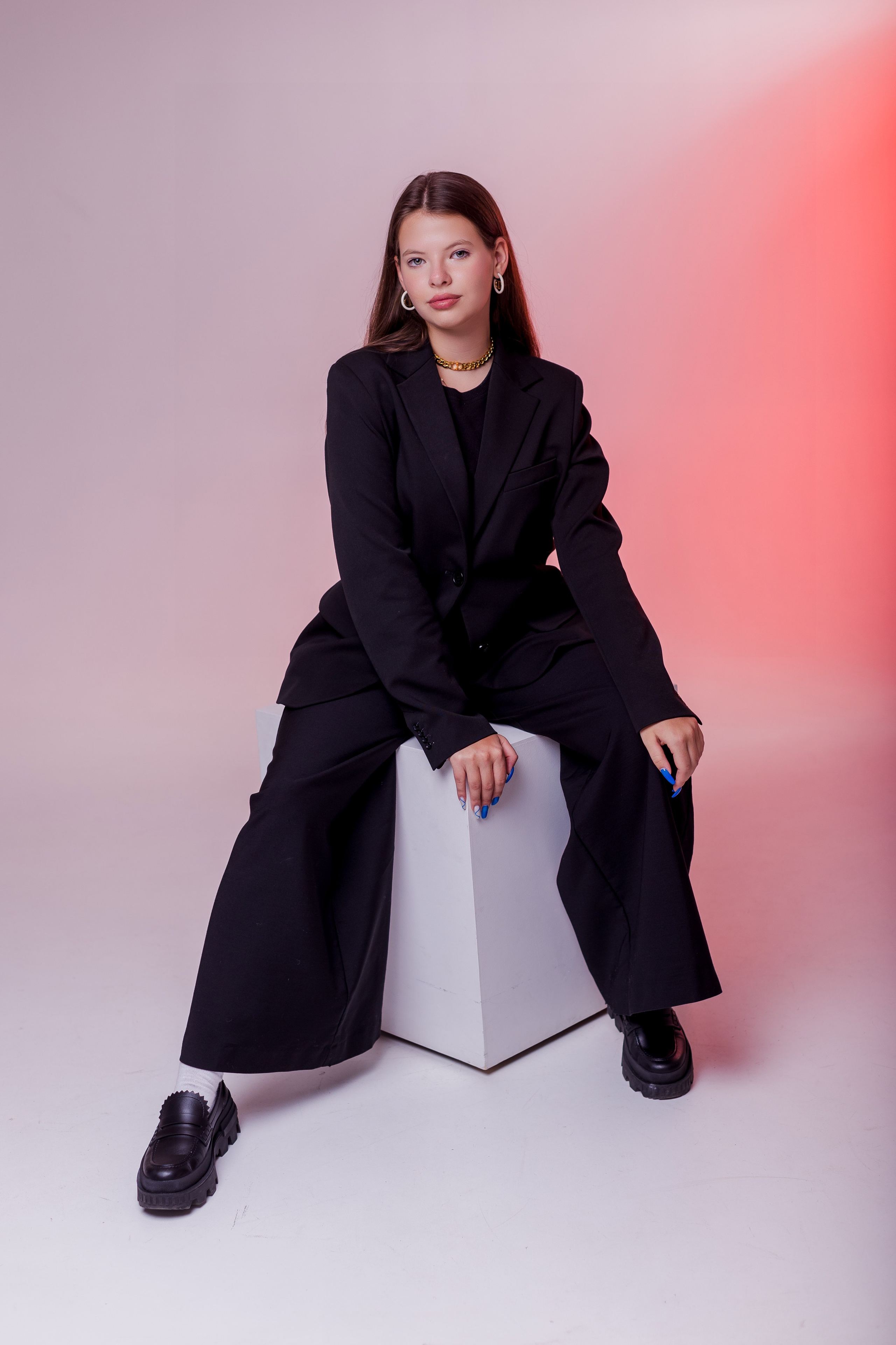 Девушка сидит на тумбе в фотостудии с цветным светом