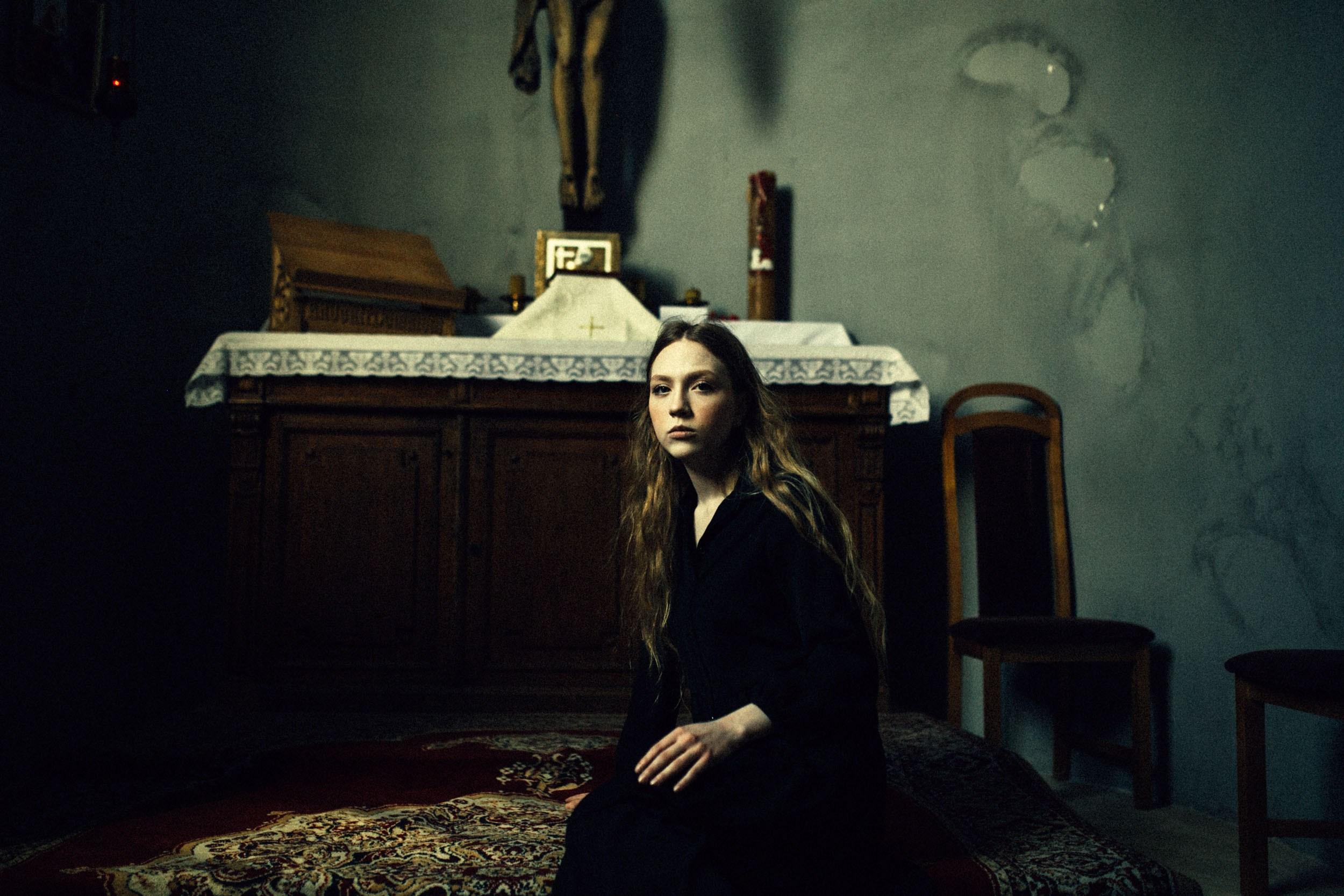 Девушка с длинными рыжими волосами в черном платье сидит у алтаря